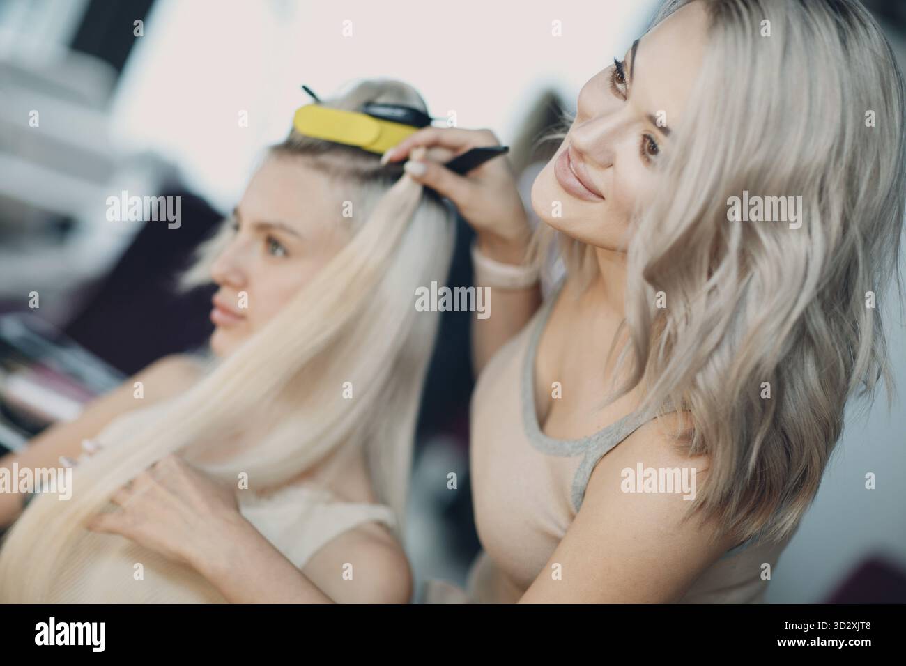 Coiffeur femme faisant des extensions de cheveux à la jeune femme avec des cheveux blonds dans le salon de beauté. Rallonge de cheveux professionnelle essayez de vérifier Banque D'Images