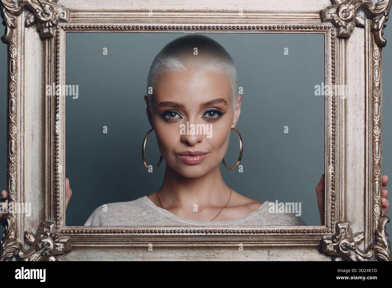 Jeune femme millénaire aux cheveux blonds courts tient le cadre doré dans les mains derrière son portrait du visage Banque D'Images