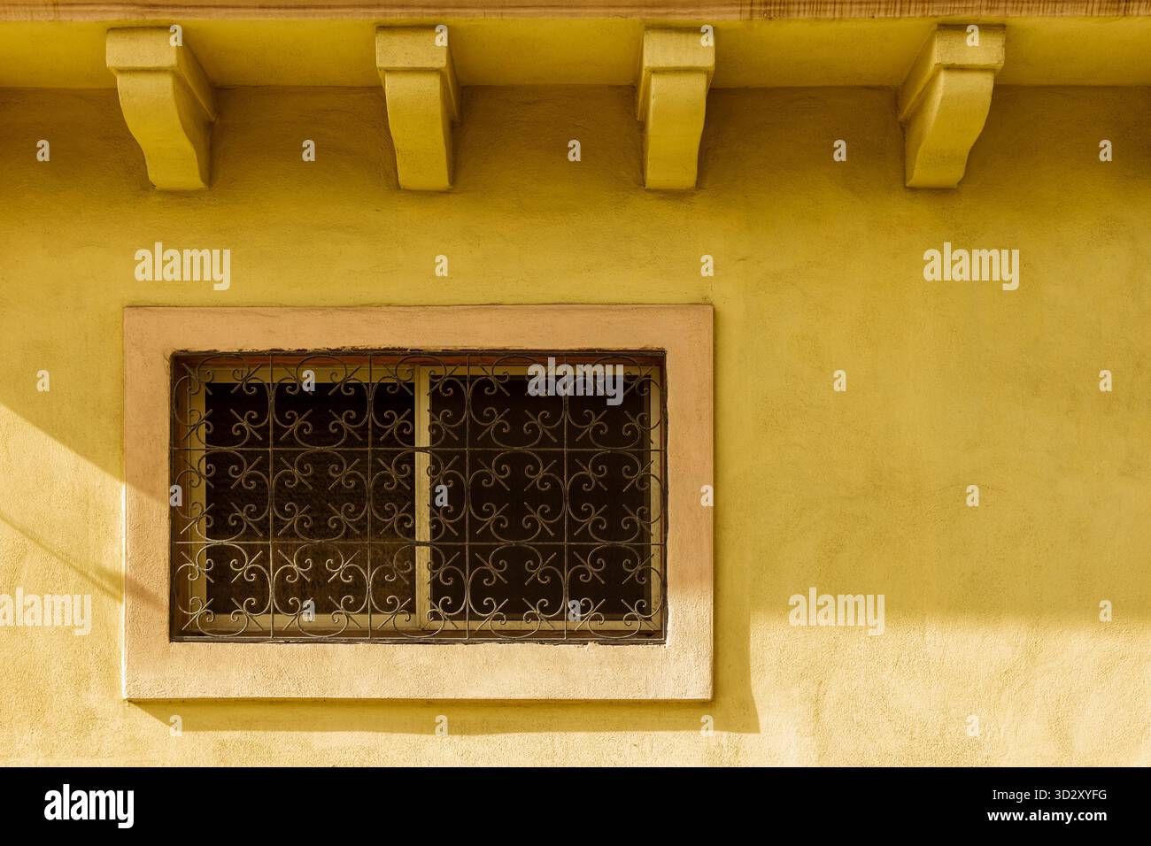 Mur jaune ensoleillé avec fenêtre décorative et grille de fer – accent architectural Banque D'Images