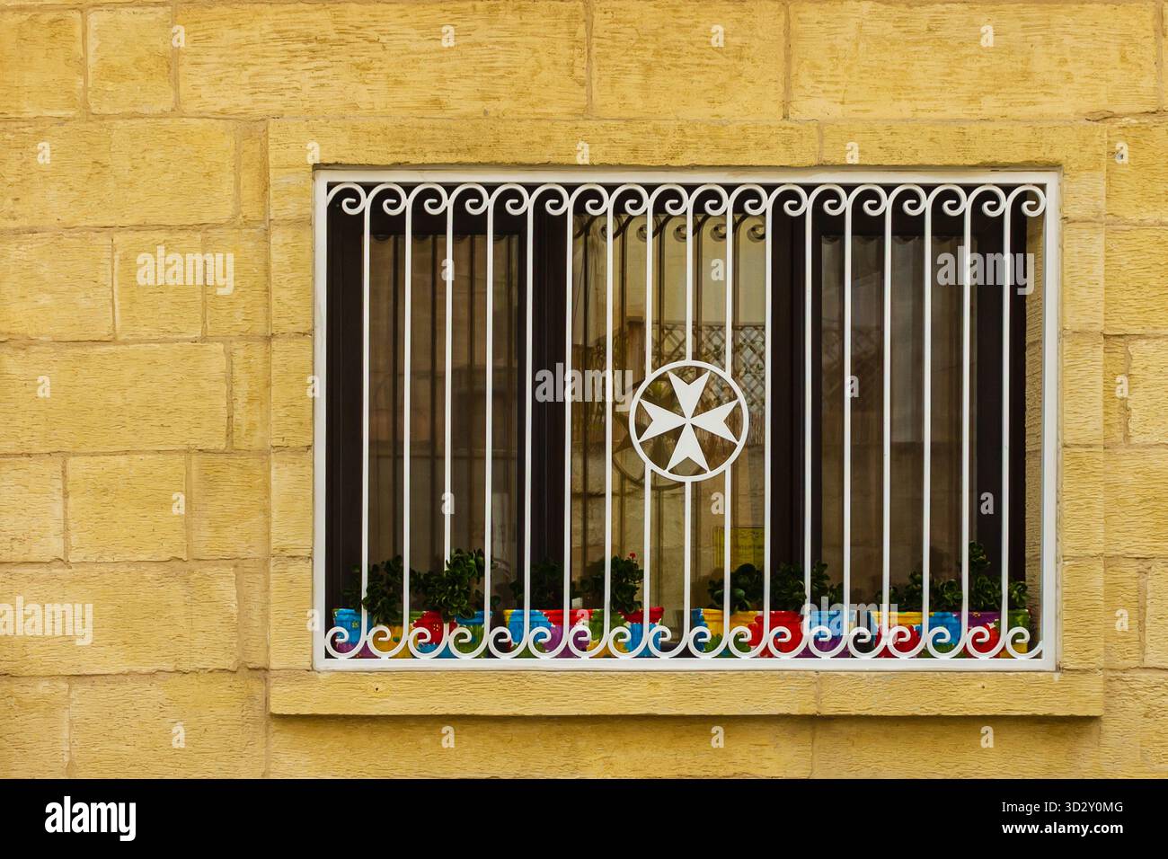 Fenêtre de bâtiment jaune avec grille décorative en fer blanc, emblème d'étoile et pots de fleurs colorés Banque D'Images