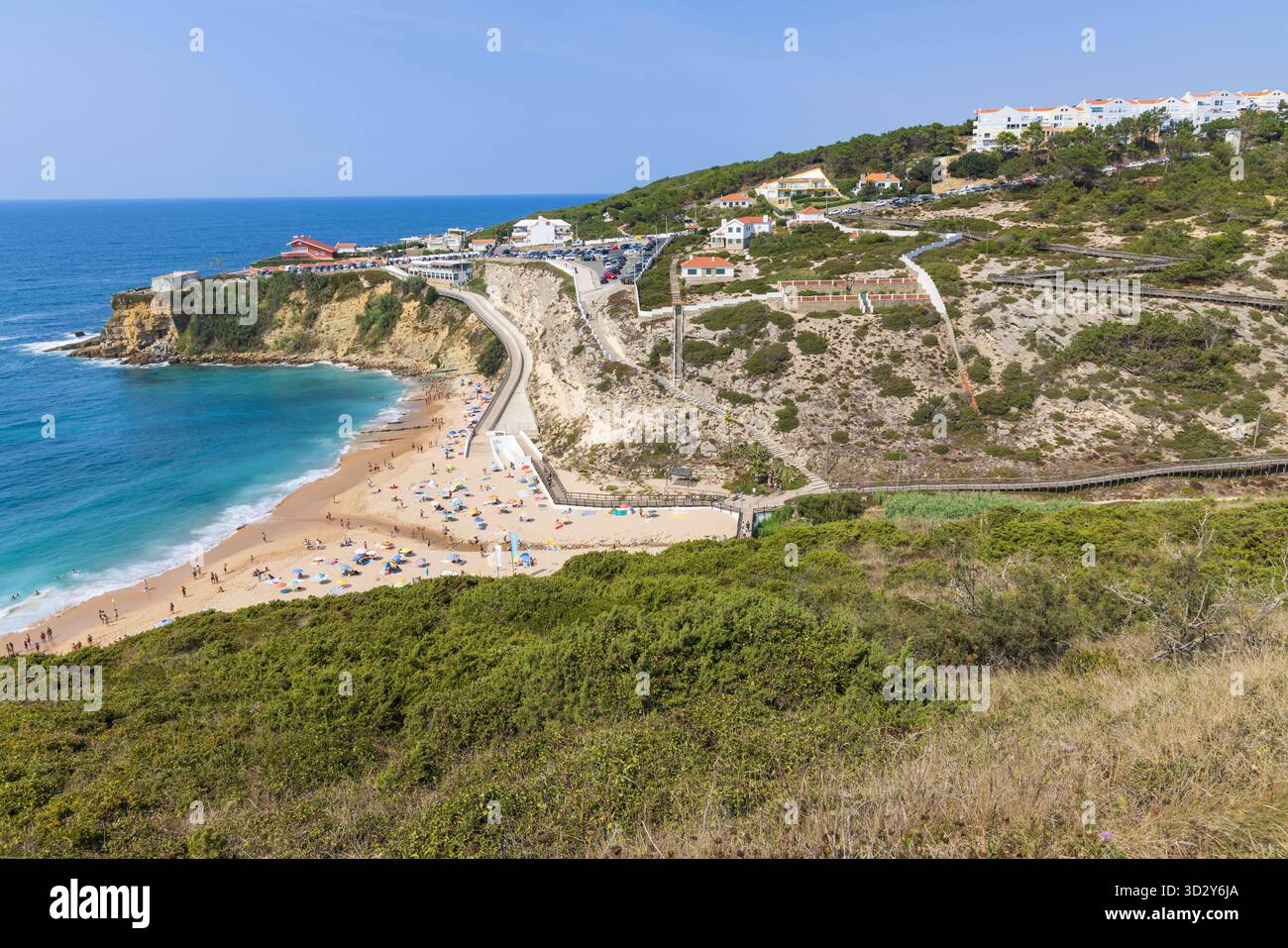 Vue surélevée de Praia do Magoito, Portugal, montrant la plage, eau turquoise, parking, route côtière, et maisons construites sur la pente verdoyante. Banque D'Images