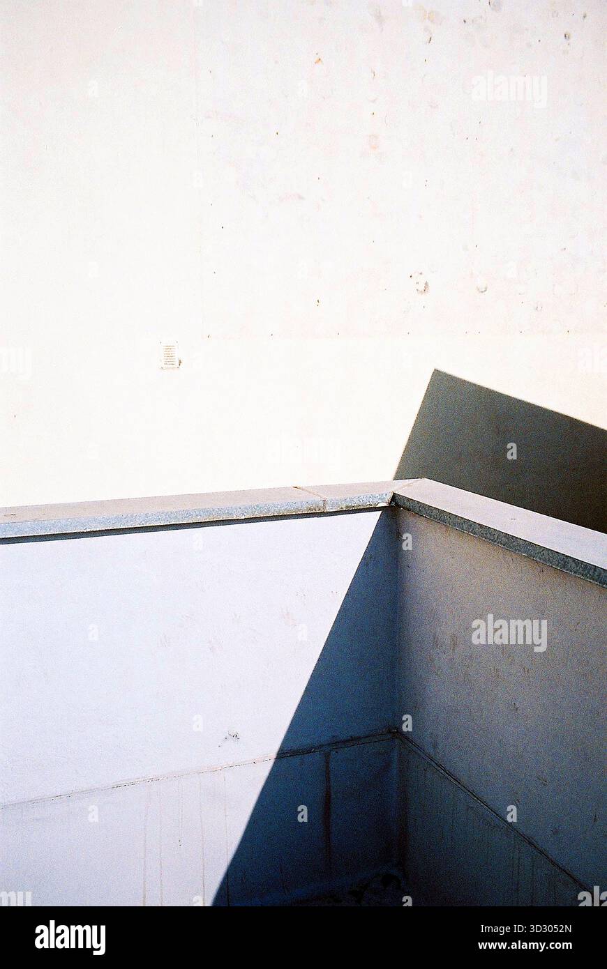 Coin terrasse en béton et mur de bâtiment à la lumière du soleil, avec des ombres formant une unité abstraite, capturée dans des tons analogiques chauds. Banque D'Images