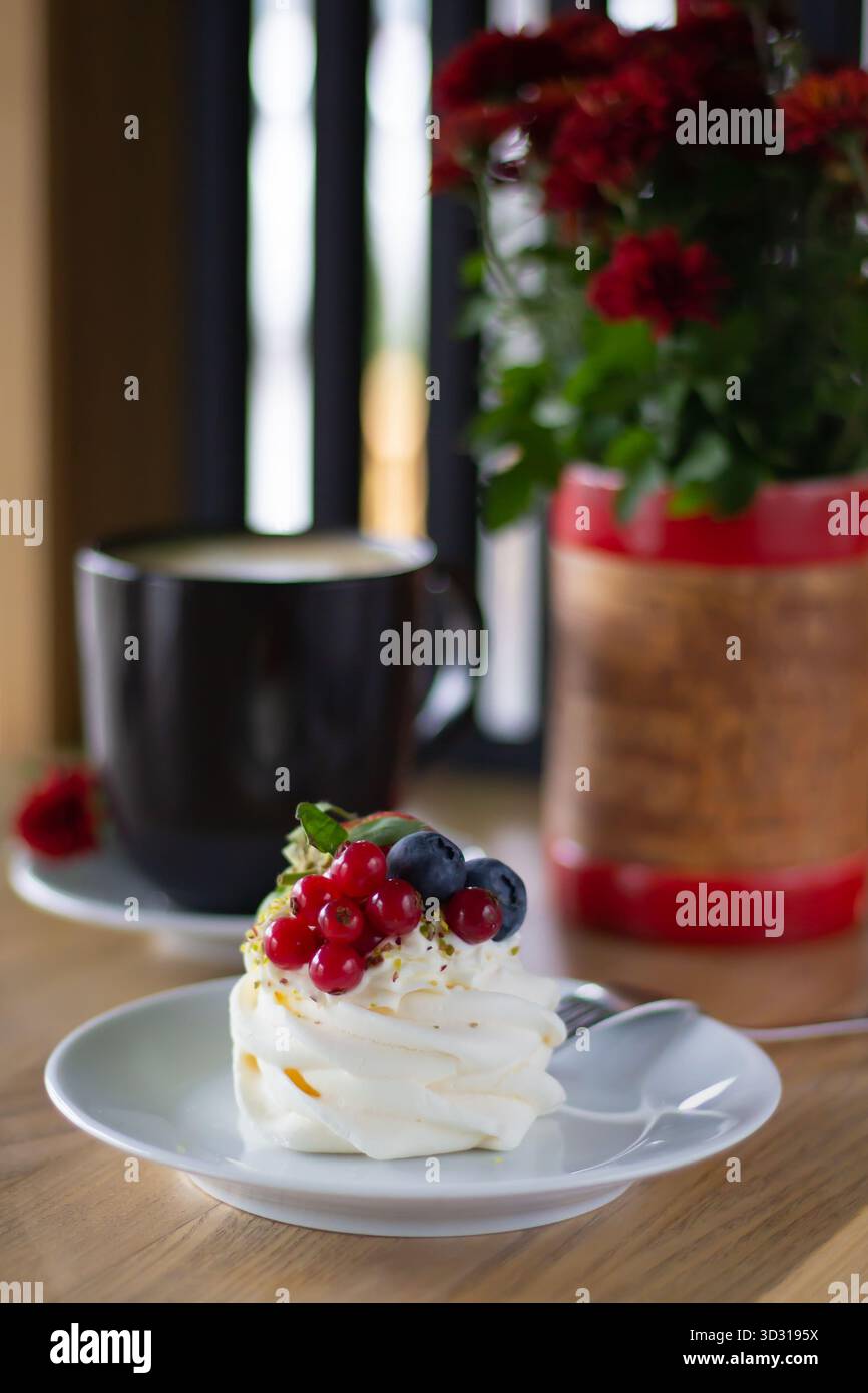 Un délicieux dessert se trouve sur une assiette blanche, ornée de baies rouges et bleues. Une tasse de café chaude et des fleurs en fleurs créent un café accueillant atmo Banque D'Images