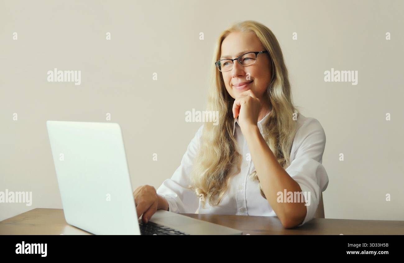 Heureuse femme mature confiante travaillant sur ordinateur portable portant des lunettes, assis au bureau au bureau ou à la maison || modèle libéré Banque D'Images