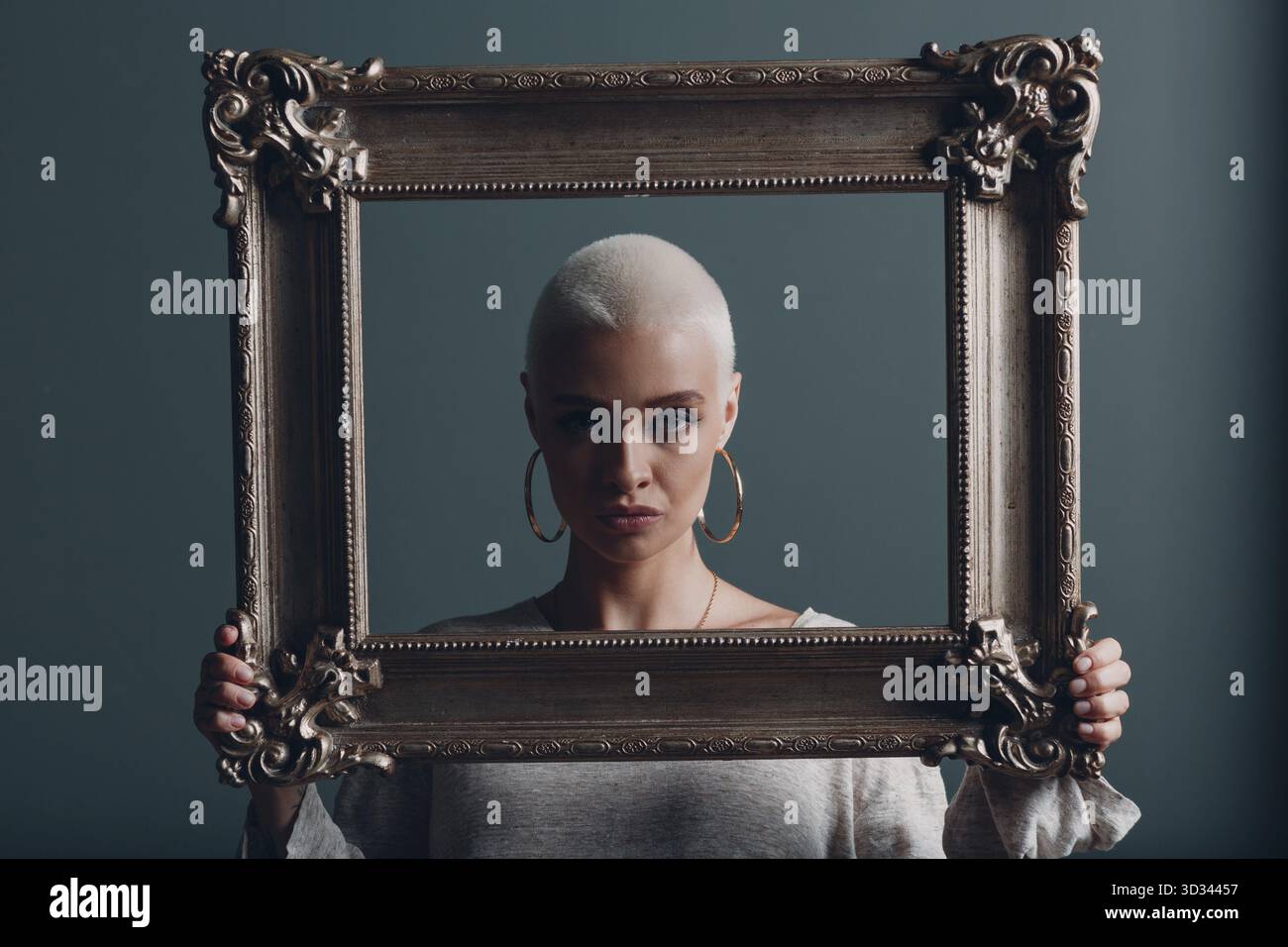 Jeune femme millénaire aux cheveux blonds courts tient le cadre doré dans les mains derrière son portrait du visage Banque D'Images