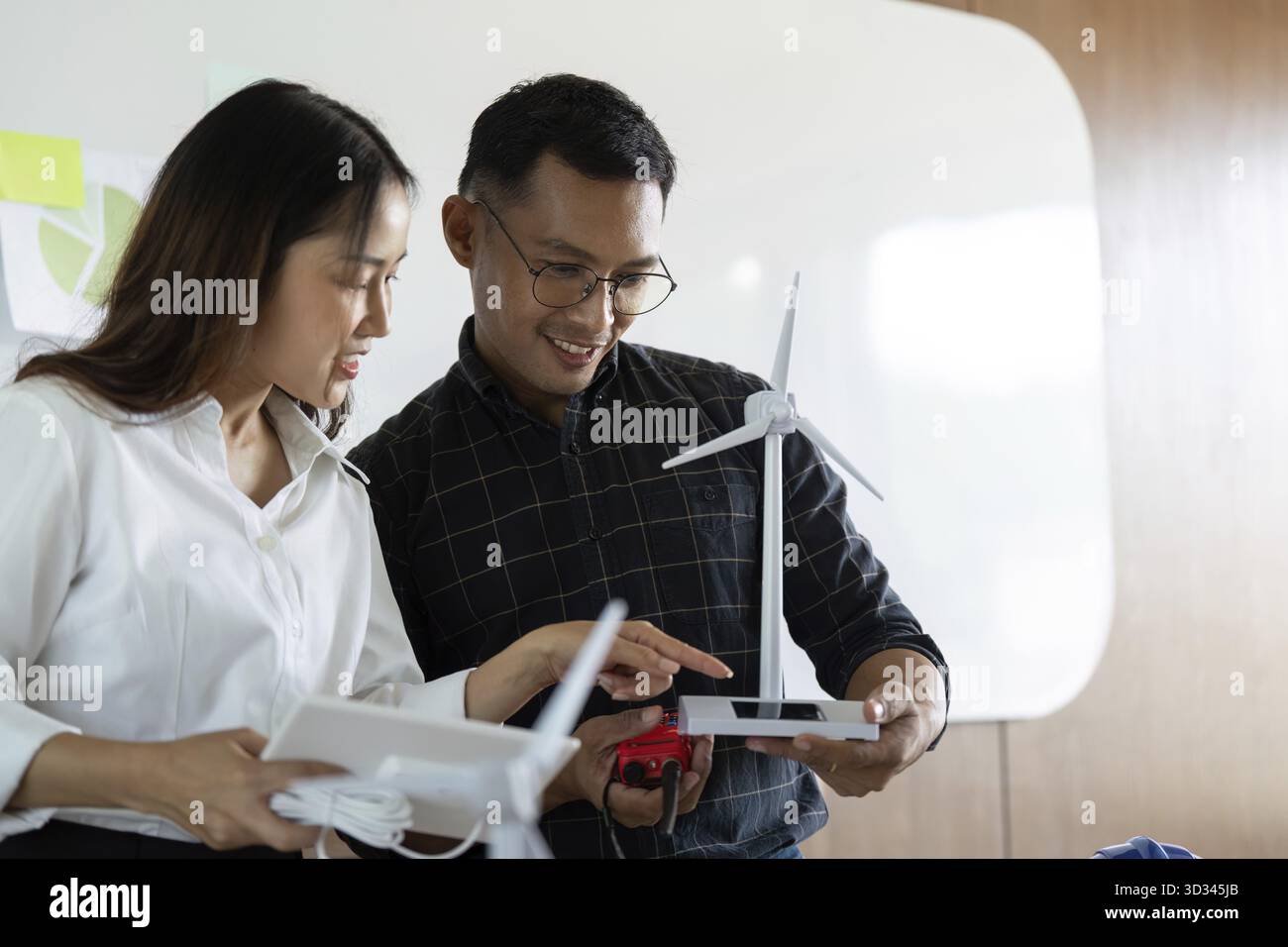 Deux ingénieurs discutent de modèles d'éoliennes et de concepts de conception durable dans un espace de travail lumineux, mettant l'accent sur le travail d'équipe et l'innovation Banque D'Images