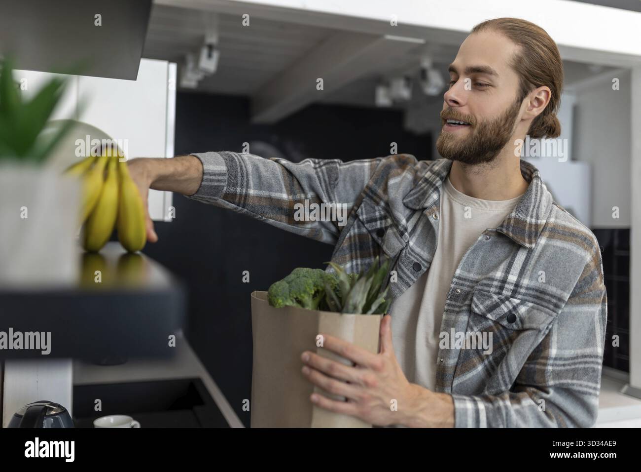Homme barbu déballant les légumes et les fruits dans la cuisine après avoir visité le magasin, achetant des produits frais Banque D'Images