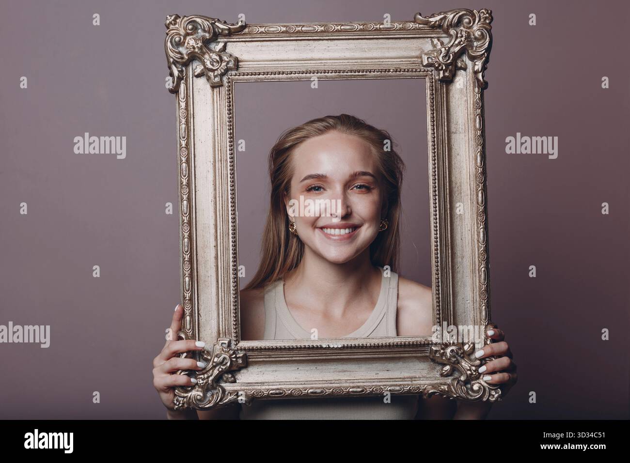 Jeune femme millénial cheveux blonds tient image dorée cadre dans les mains visage portrait Banque D'Images