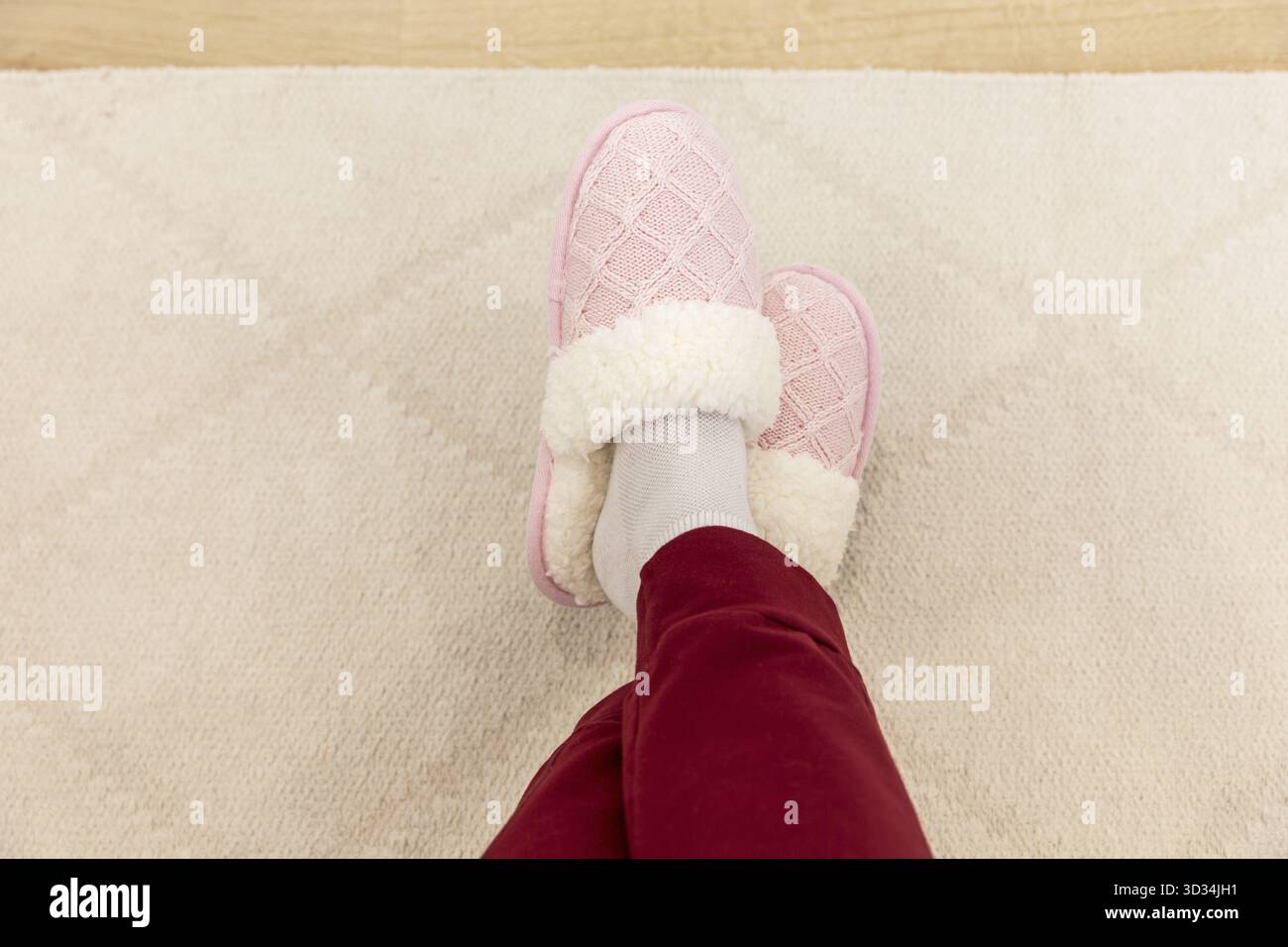 Jambes croisées portant des pantoufles tricotées roses Banque D'Images