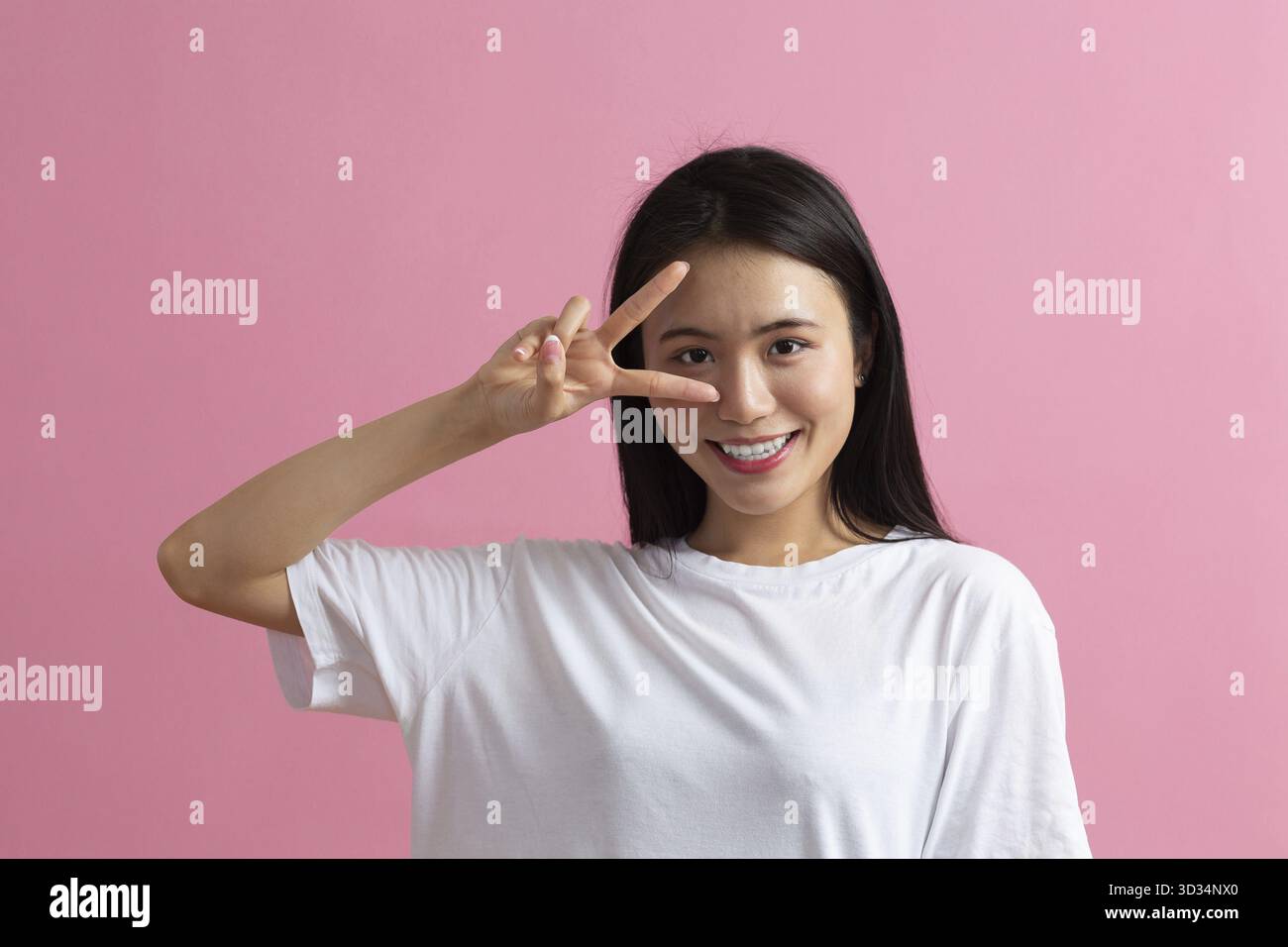 Portrait de femme souriante positive asiatique avec geste en V Fingers sur fond rose Banque D'Images