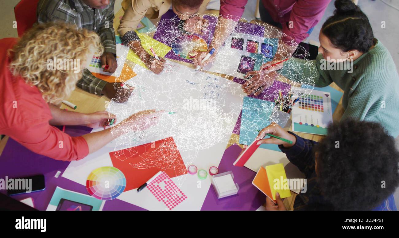 Équipe de conception collaboratrice se penchant autour de la table dans le studio, passant la roue de couleur et des échantillons de peinture Banque D'Images