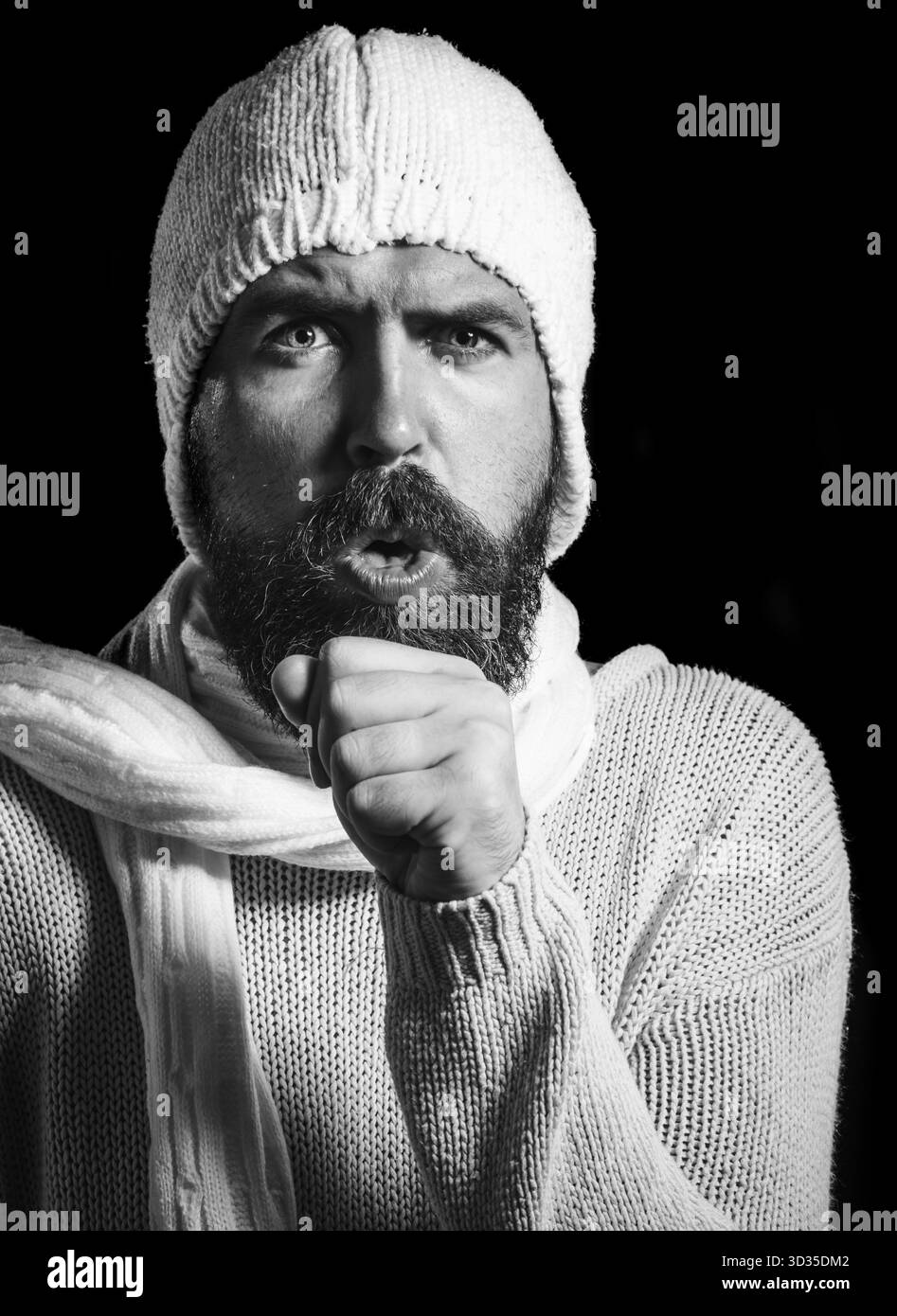 Homme barbu en pull, écharpe et chapeau toussant ayant froid. Beau gars en vêtements chauds souffrant de mal de gorge. Maladie, médecine, traitement, santé Banque D'Images