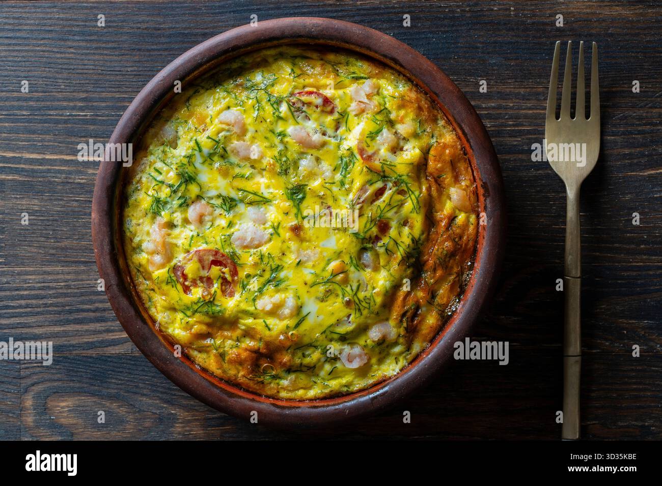 Bol en céramique avec frittata de légumes, nourriture simple. Frittata avec oeuf, tomate, poivre, oignon, crevettes et fromage sur table en bois, gros plan, vue de dessus. I Banque D'Images
