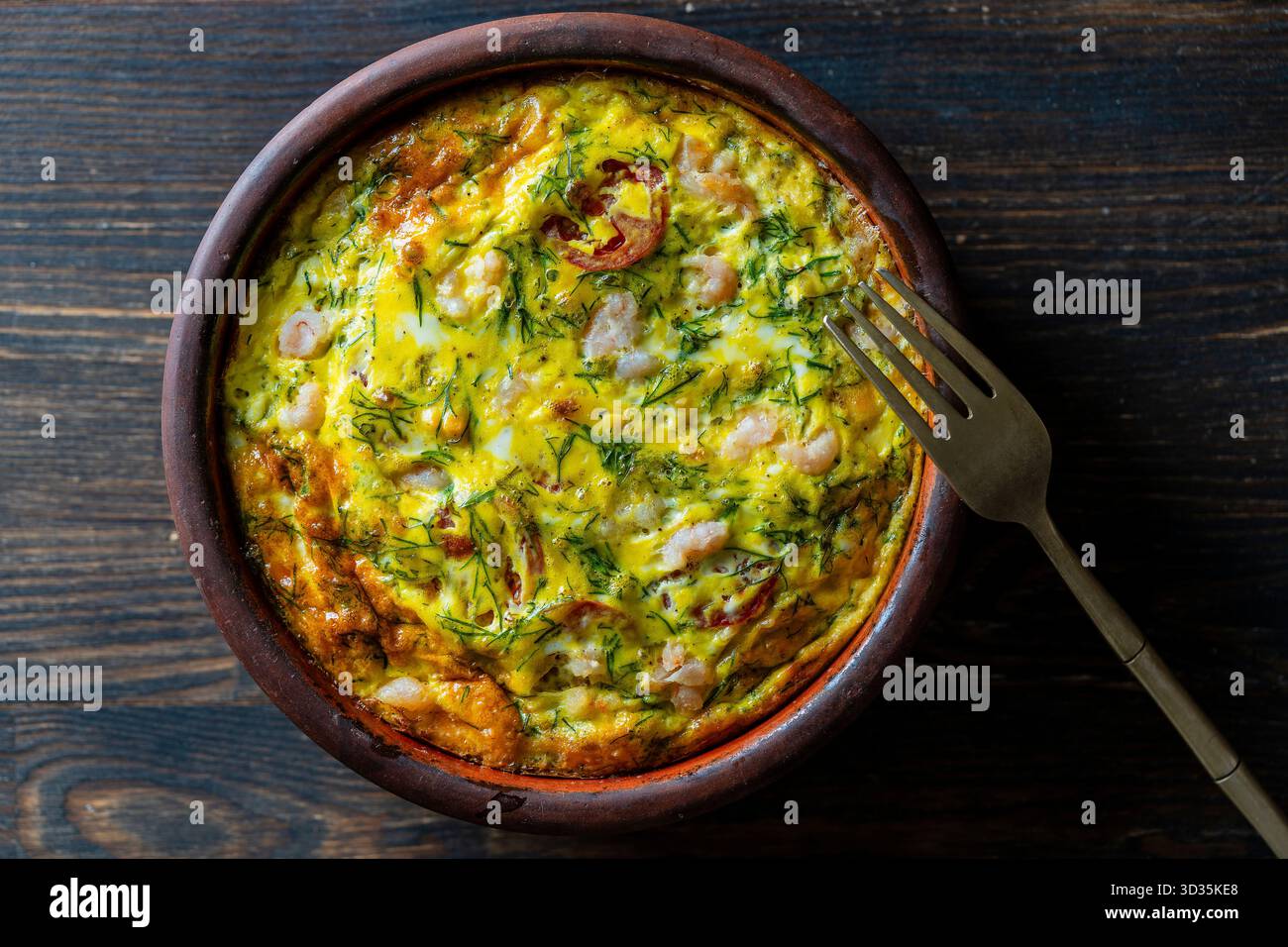 Bol en céramique avec frittata de légumes, nourriture simple. Frittata avec oeuf, tomate, poivre, oignon, crevettes et fromage sur table en bois, gros plan, vue de dessus. I Banque D'Images