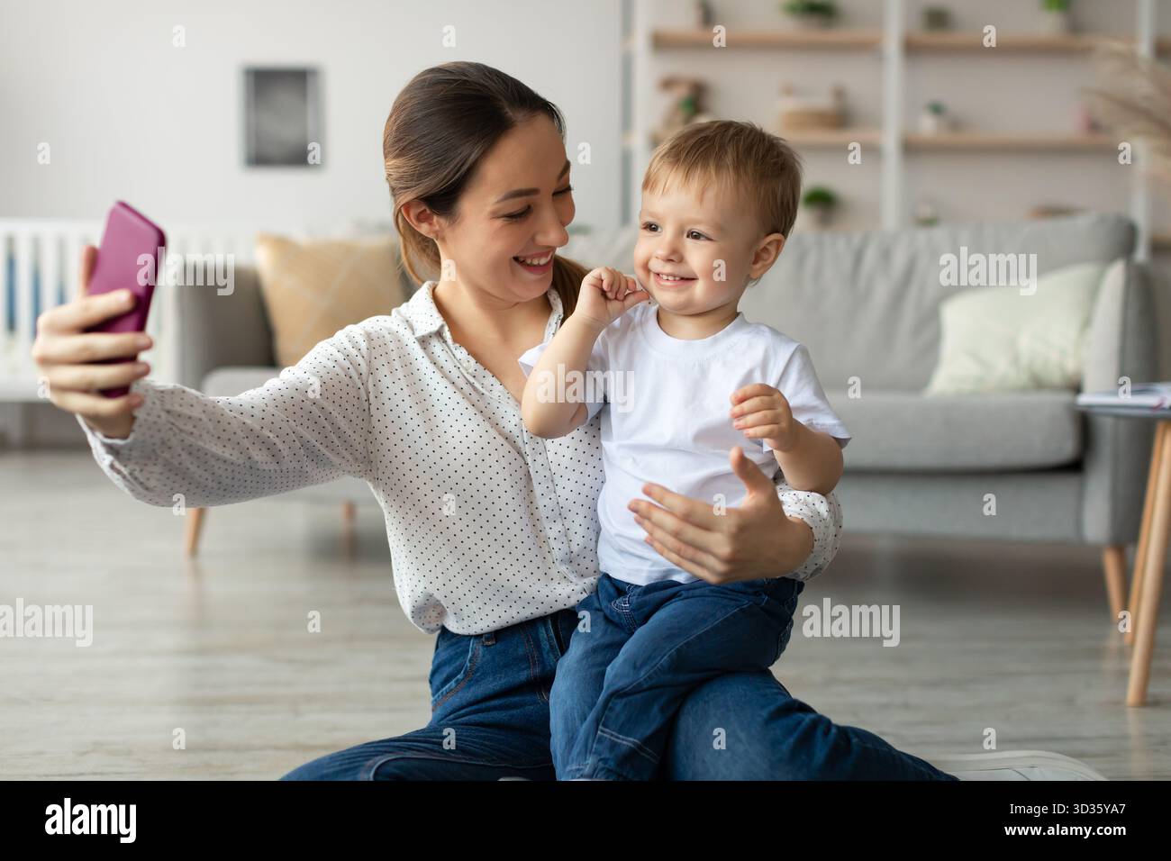 Mère et fils s'amusant ensemble tout en prenant un Selfie à la maison dans un salon chaleureux et accueillant Banque D'Images