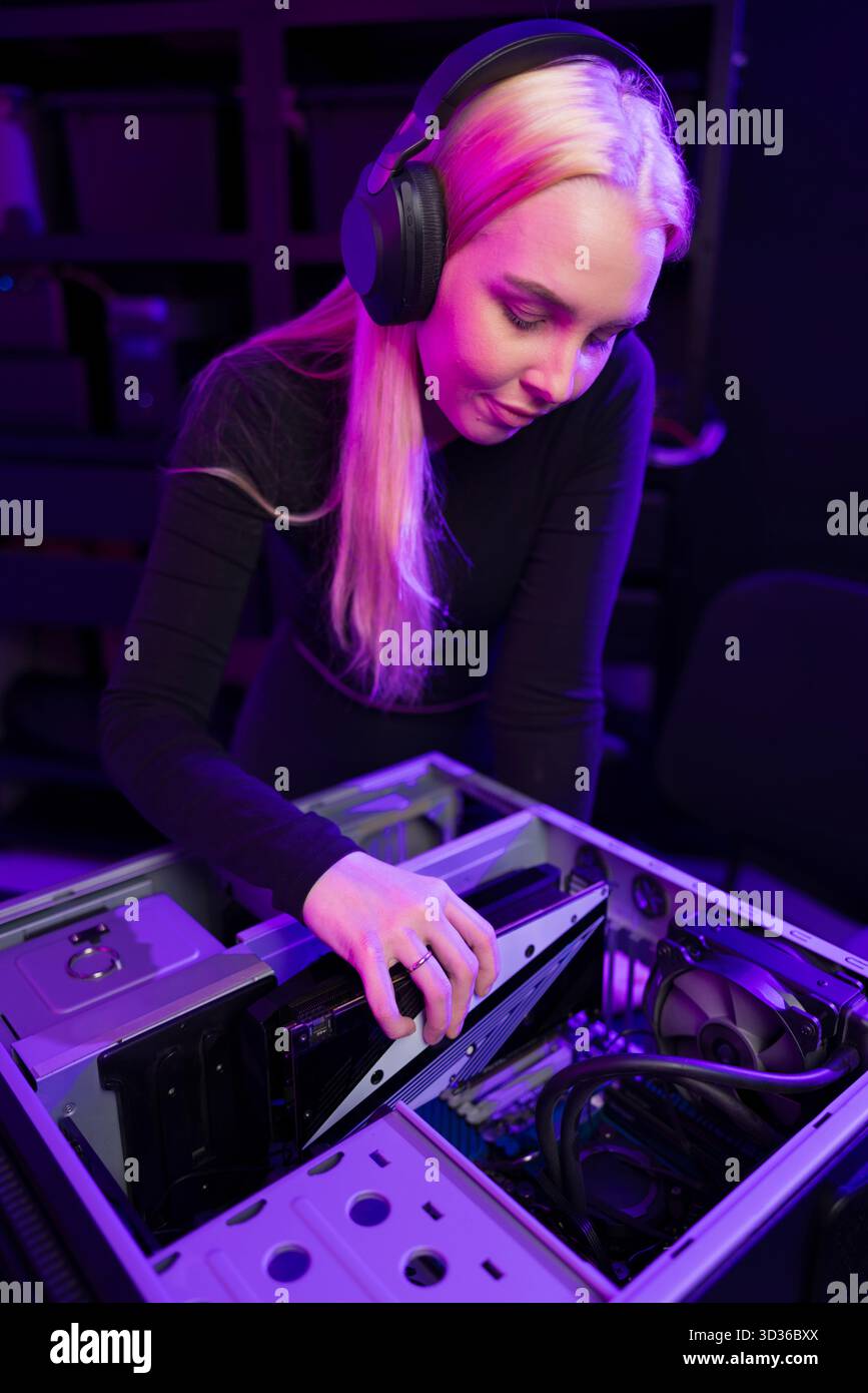 Jeune femme joueuse met à niveau un PC de jeu, personnalisant le matériel avec l'accent dans une configuration high-tech Banque D'Images