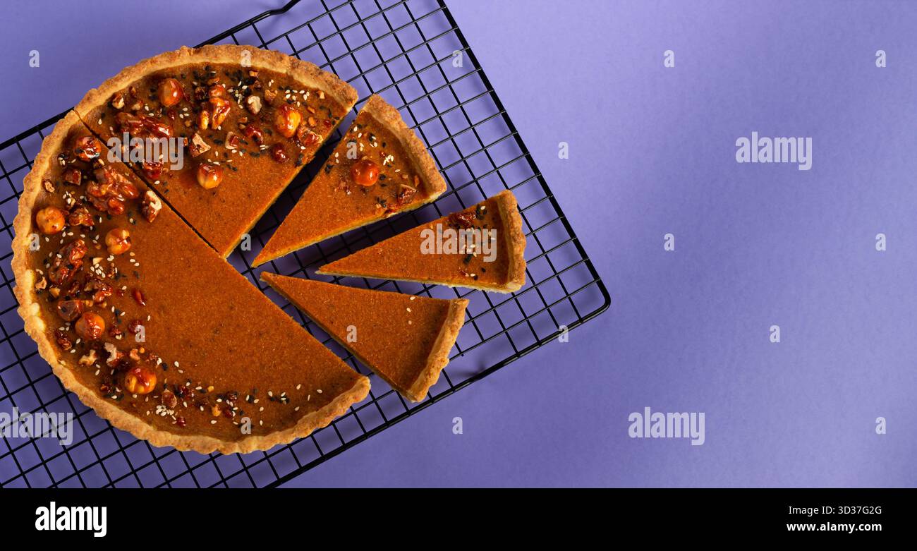 Une tarte à la citrouille fraîchement cuite se trouve sur une grille de refroidissement métallique, coupée en morceaux. La tarte est garnie de noix et de graines, invitant le plaisir à un gathe confortable Banque D'Images
