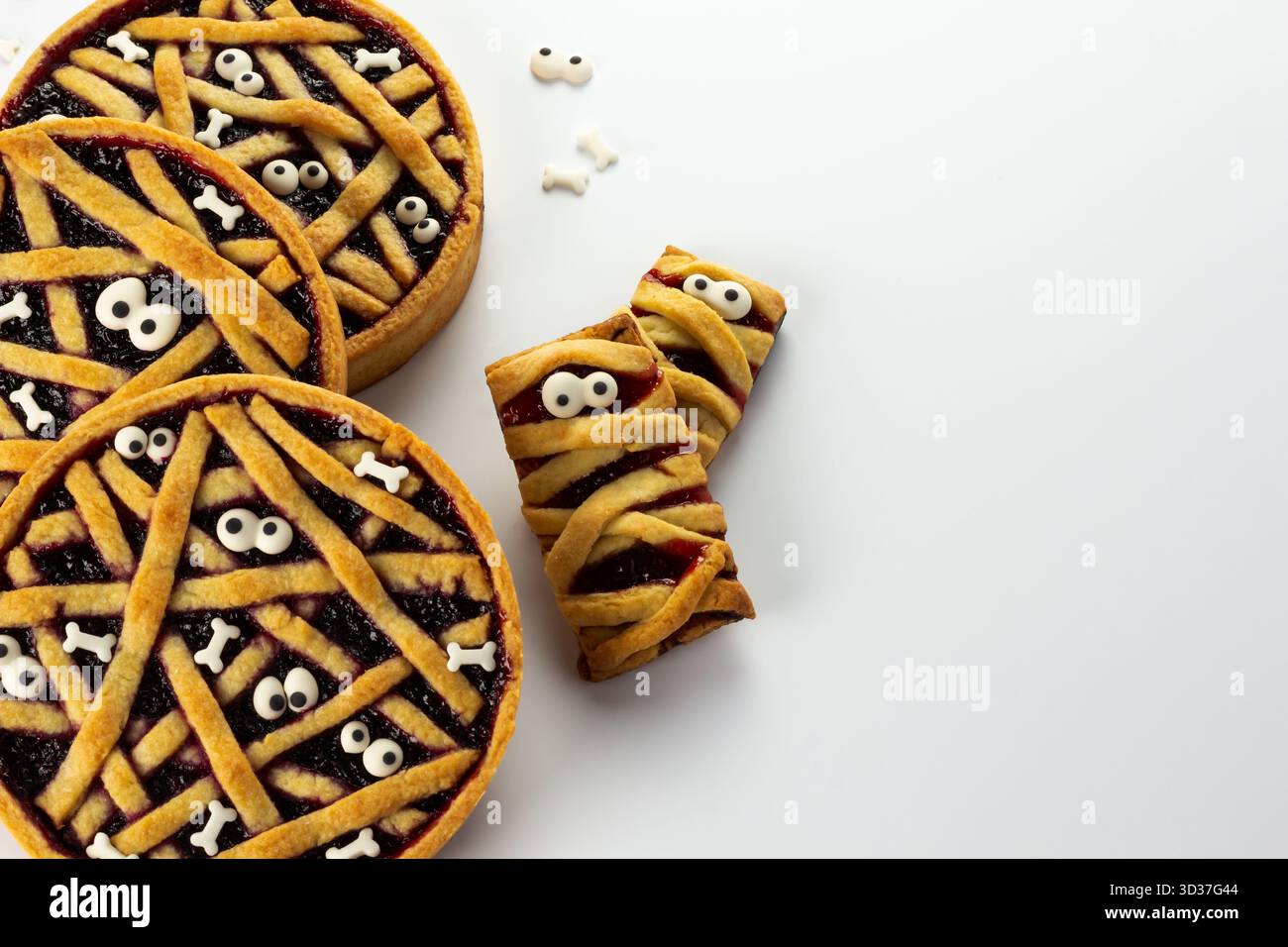 Les délicieux desserts d'Halloween présentent des coquilles de tarte remplies de confiture de baies, surmontées de motifs en treillis et d'yeux de bonbons effrayants. Parfait pour les rassemblements festifs Banque D'Images