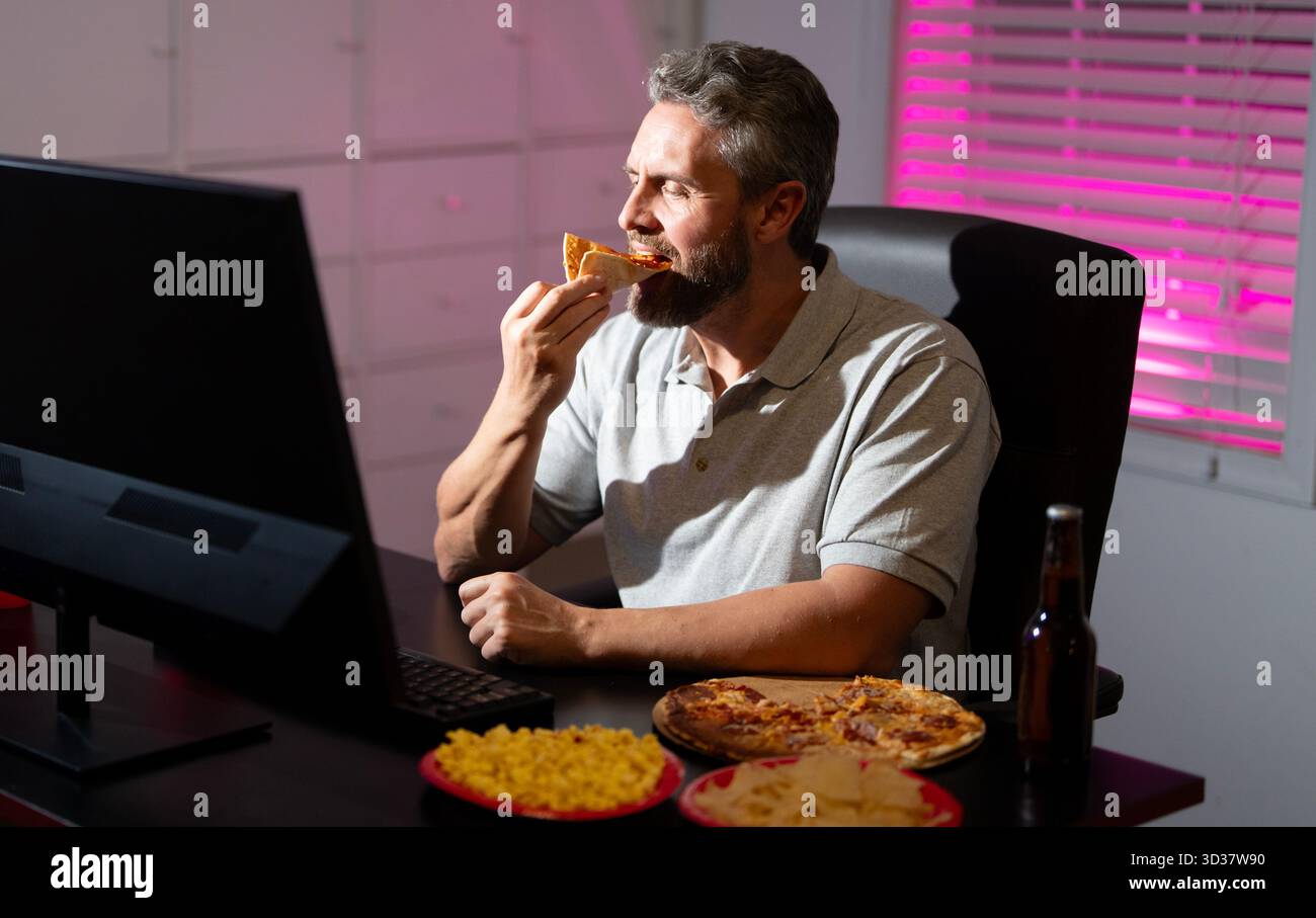 Homme d'affaires manger de la pizza en heures supplémentaires. Homme occupé mangeant le dîner et travaillant en ligne au bureau de nuit. Entrepreneur travaille tard dans la nuit tout en dégustant une collation. A Banque D'Images