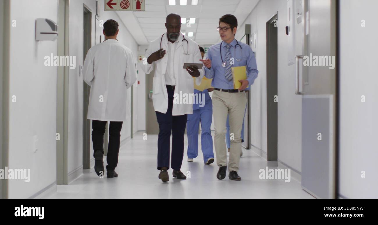 Les médecins masculins marchants vérifiant la tablette dans le couloir de l'hôpital, avec des blouses de laboratoire et des stéthoscopes Banque D'Images