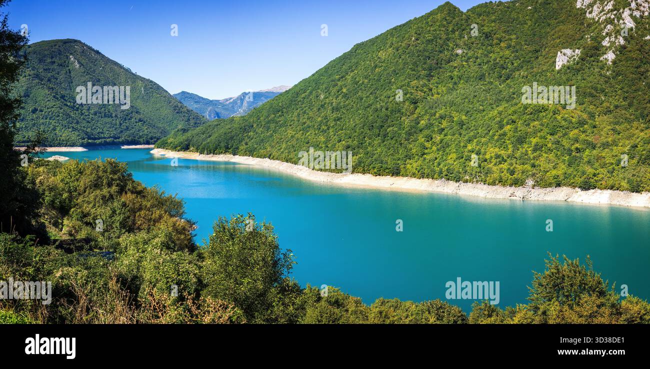 Vue panoramique sur le lac Piva au Monténégro entouré de montagnes vertes abruptes et de falaises rocheuses sous un ciel bleu clair reflétant dans une eau turquoise calme Banque D'Images