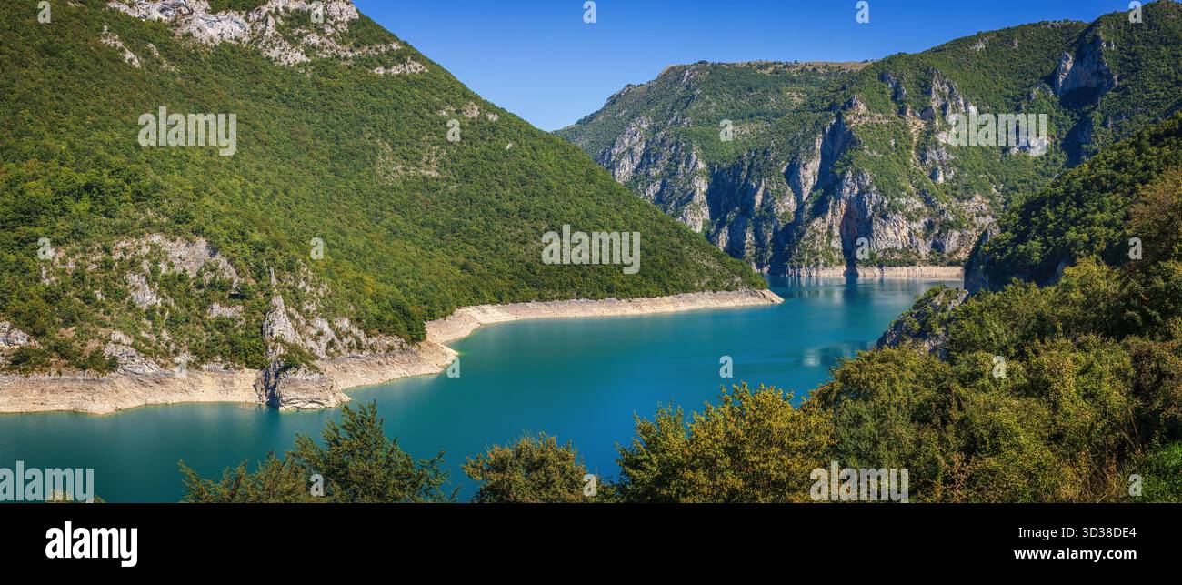 Vue panoramique sur le lac Piva au Monténégro entouré de montagnes vertes abruptes et de falaises rocheuses sous un ciel bleu clair reflétant dans une eau turquoise calme Banque D'Images
