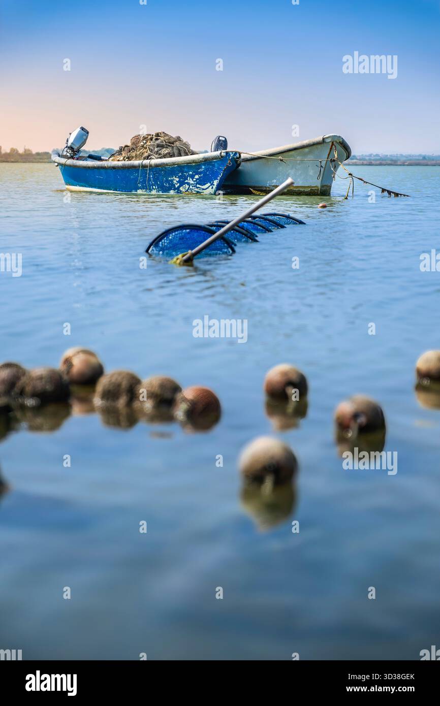 Vue rapprochée de flotteurs en liège flottants et d'un filet submergé, avec un bateau de pêche bleu et blanc ancré dans l'étang de Canet, France Banque D'Images