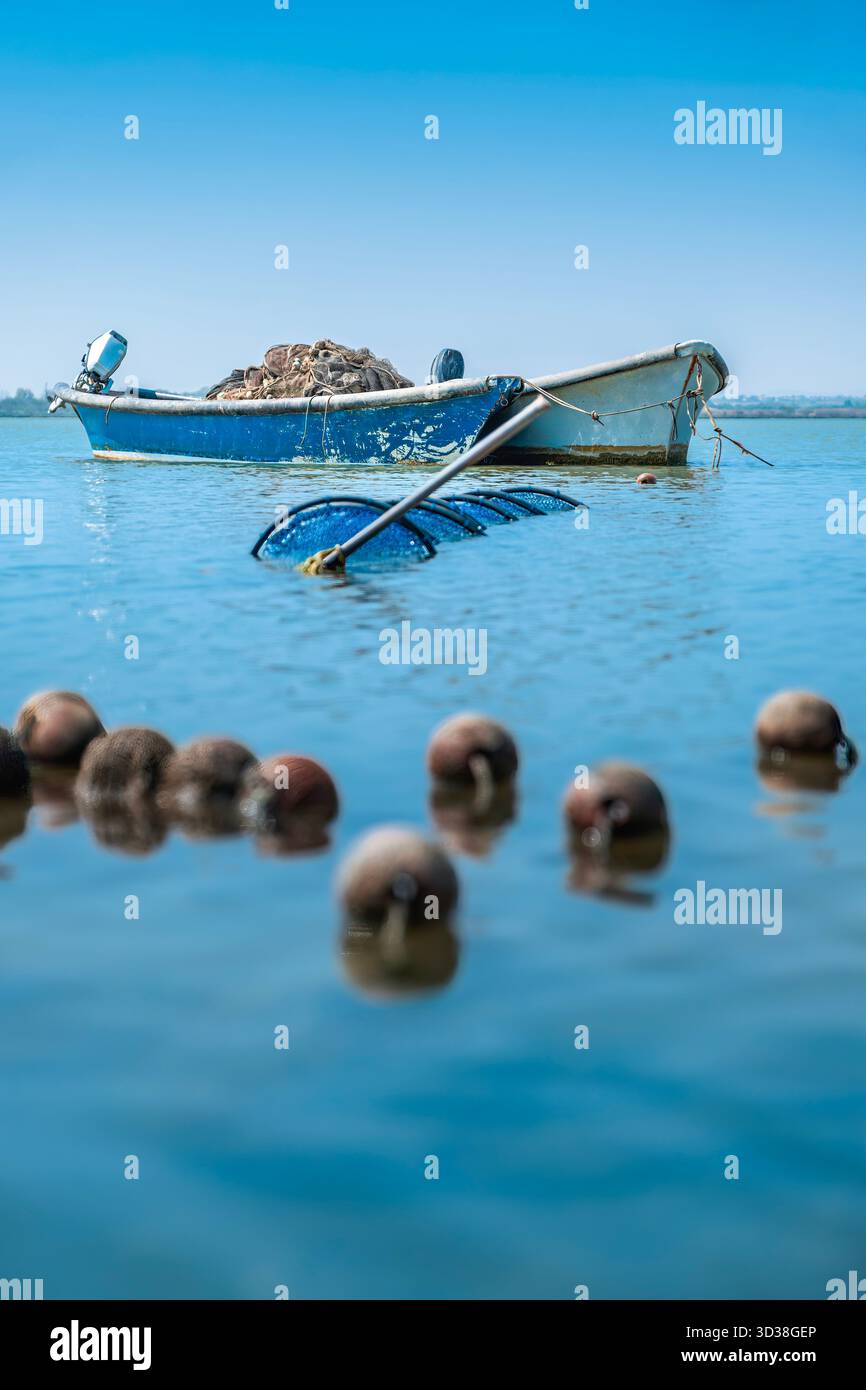 Focus peu profond sur le liège flottant flotte en eau claire, avec un bateau de pêche bleu et un filet cylindrique submergé en arrière-plan, France Banque D'Images