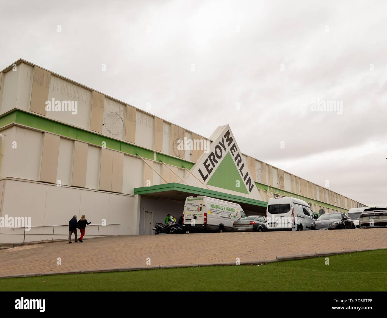 Extérieur du bâtiment de vente au détail avec les clients marchant vers l'entrée et les véhicules garés devant sous un ciel nuageux Banque D'Images