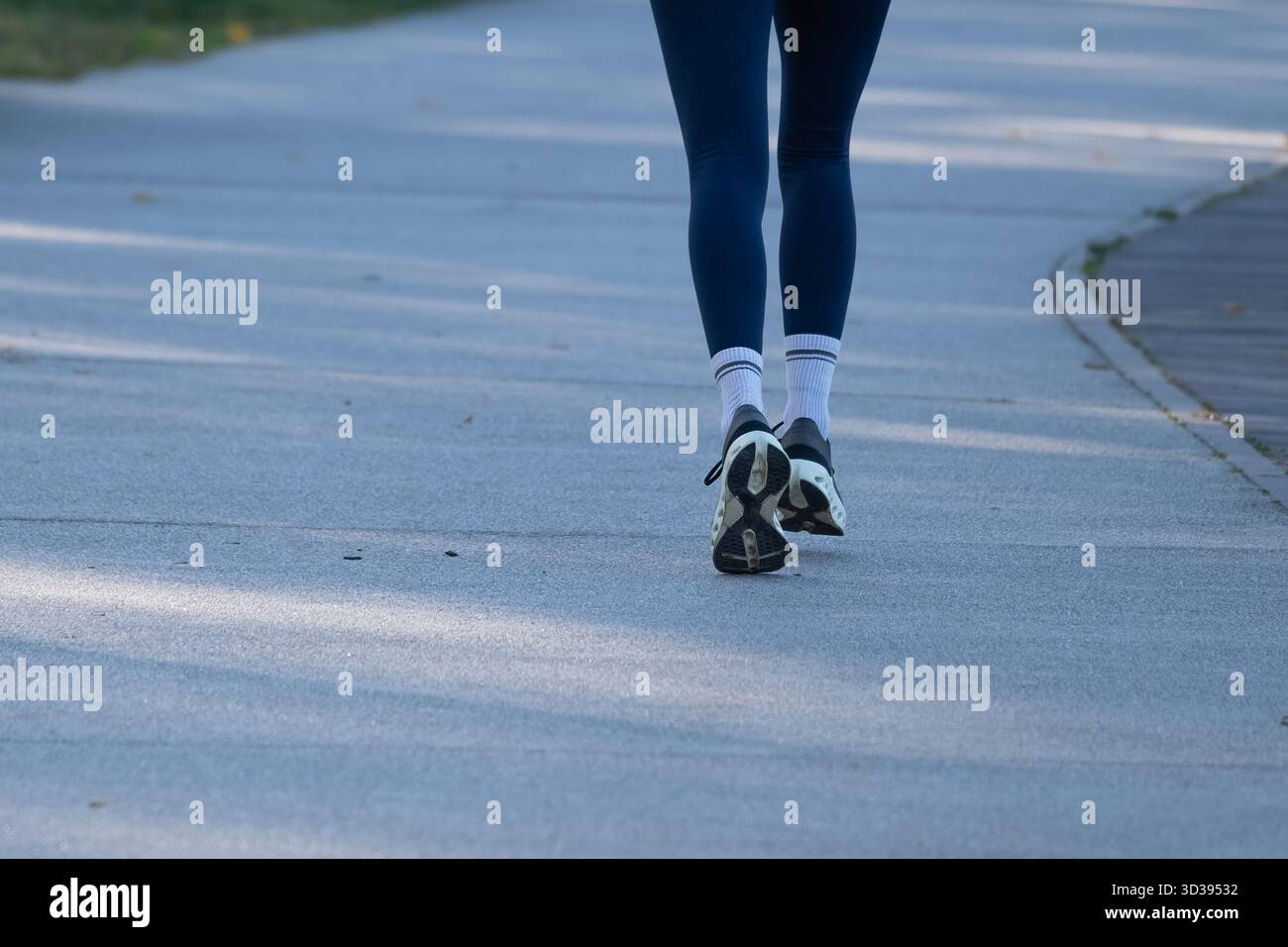 Vue arrière d'une personne marchant sur un chemin de parc pavé en vêtements de sport et chaussures de course. Concept de style de vie actif adapté au fitness, au bien-être, au par urbain Banque D'Images