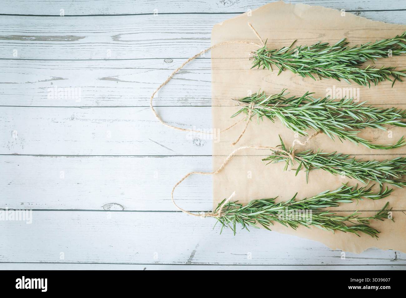 Quatre paquets de romarin préparés pour le séchage, stylisés sur papier parchemin avec fond en bois de ferme. Parfait pour les recettes saisonnières ou l'artisanat à base de plantes Banque D'Images