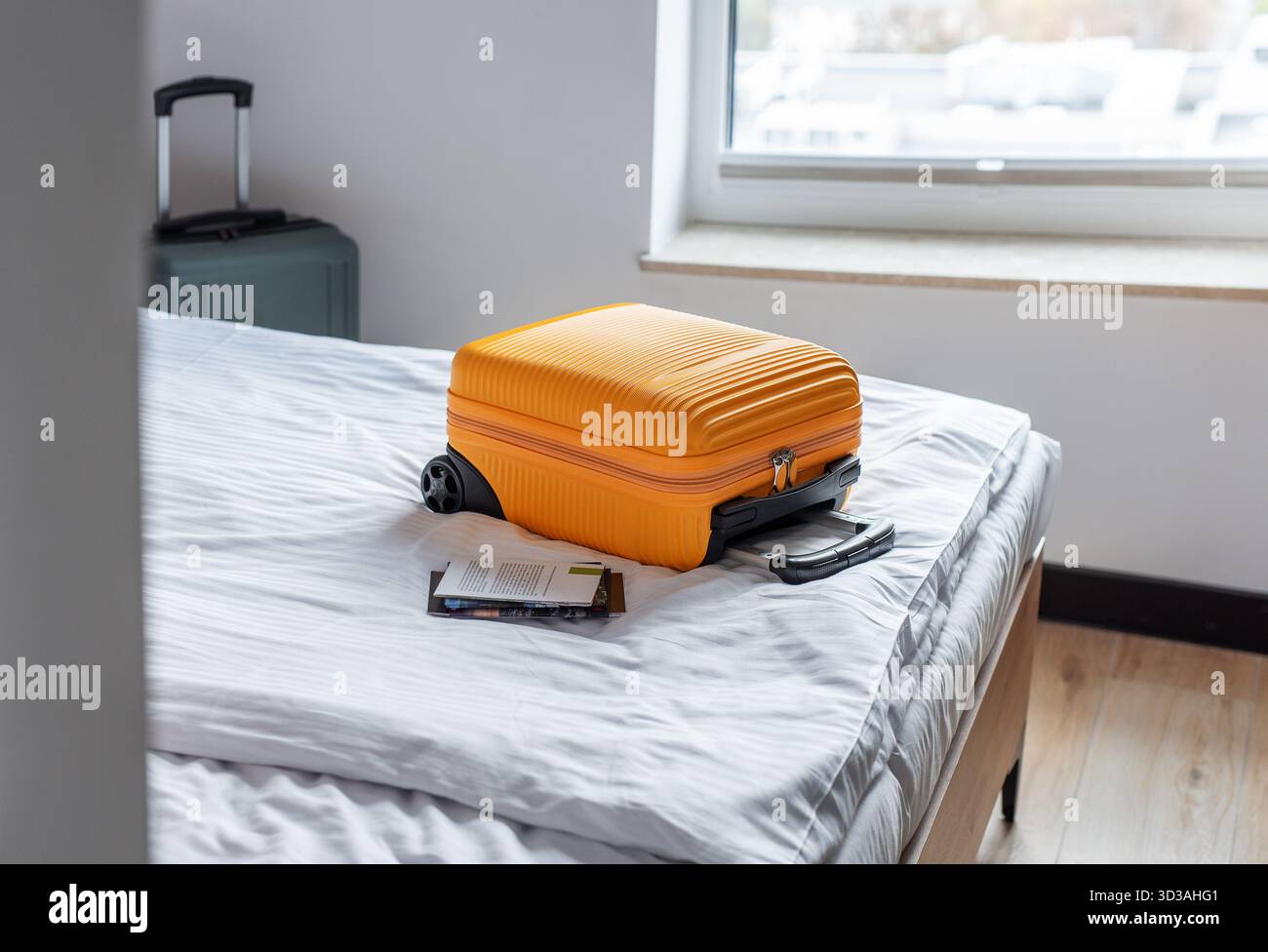 Valise orange et brochure imprimée reposant sur le lit d'hôtel, symbolisant voyage et vacances Banque D'Images