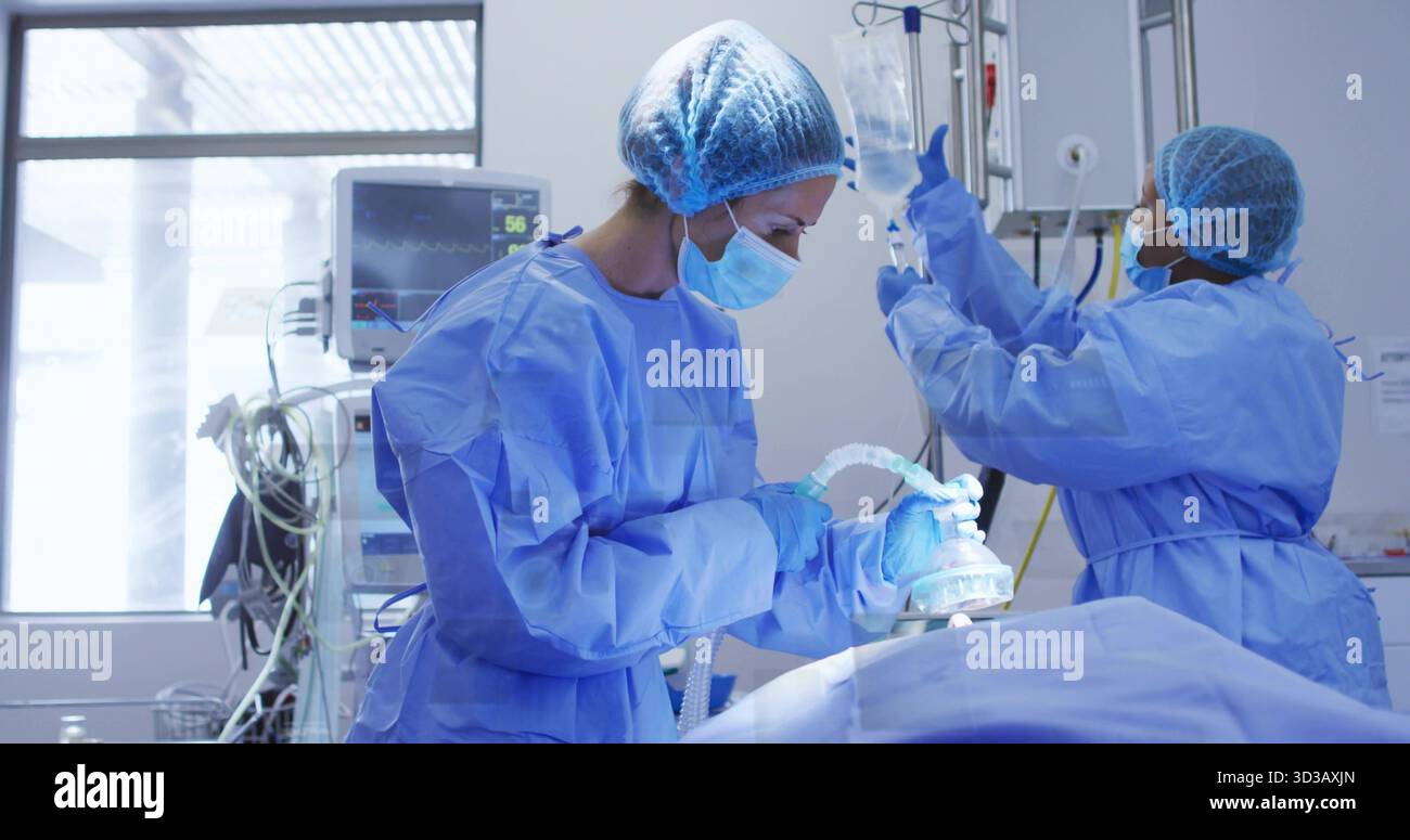 Chirurgien opérateur tenant le masque d'anesthésie au-dessus du patient dans le BLOC OPÉRATOIRE, avec assistant ajustant la poche de liquide IV Banque D'Images