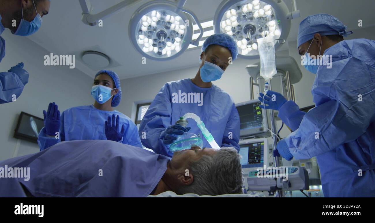 Le port du masque d'anesthésie a frotté l'équipe chirurgicale de surveillance des paramètres vitaux et d'ajustement IV au bloc opératoire Banque D'Images
