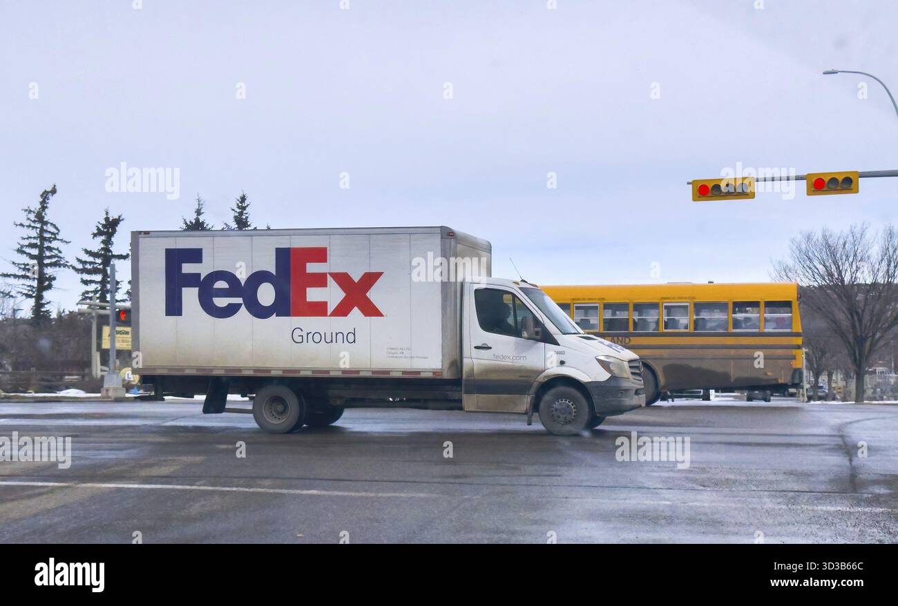 Calgary, Alberta, Canada. 2 mars 2025. Un camion de livraison terrestre FedEx blanc capturé dans un cadre urbain, avec un autobus scolaire jaune en arrière-plan. T Banque D'Images