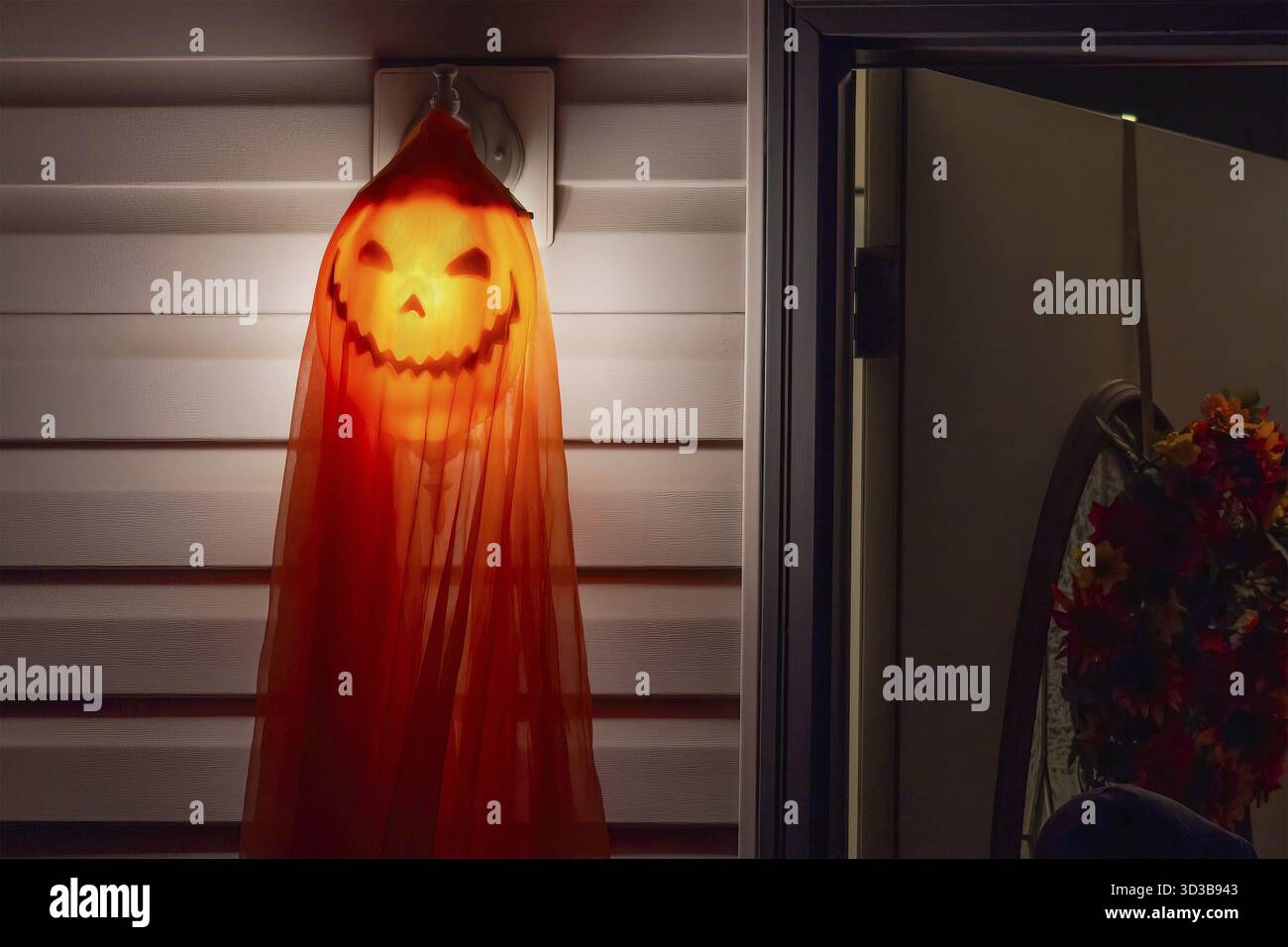 Une décoration d'Halloween effrayante pend près d'une porte, projetant une lueur étrange. Une lanterne de citrouille, partiellement obscurcie par un tissu orange, crée un mysterio Banque D'Images