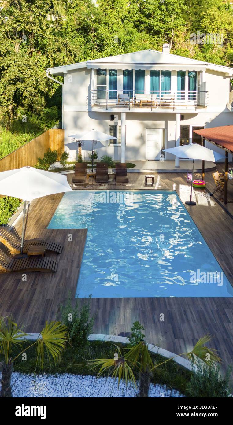 Arrière-cour moderne avec piscine, terrasse en bois et verdure luxuriante entourant une élégante maison de deux étages Banque D'Images