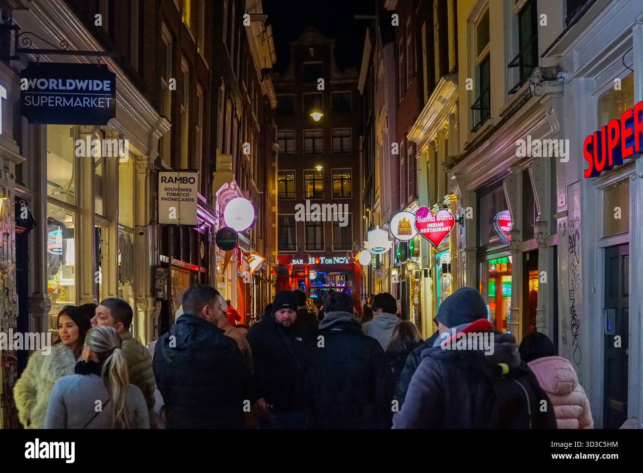 La foule remplit une rue étroite du quartier rouge d'Amsterdam la nuit, entourée de néons, de bars et de restaurants internationaux. Banque D'Images