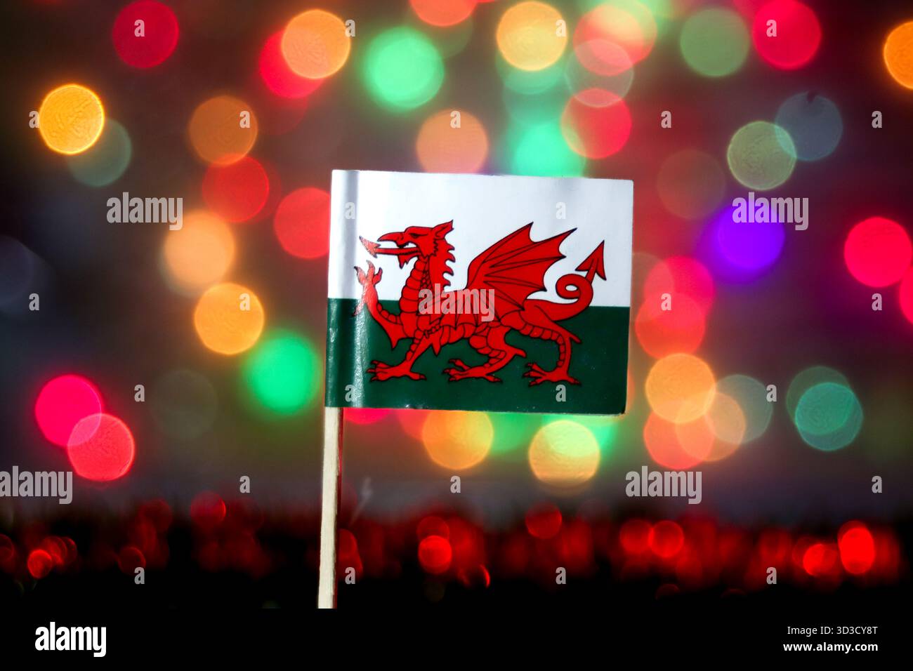 Détail du drapeau gallois (y Ddraig Goch) contre un bokeh coloré. Idéal pour la fierté nationale, les célébrations, le tourisme au Royaume-Uni et les grands événements sportifs comme le rugby. Banque D'Images