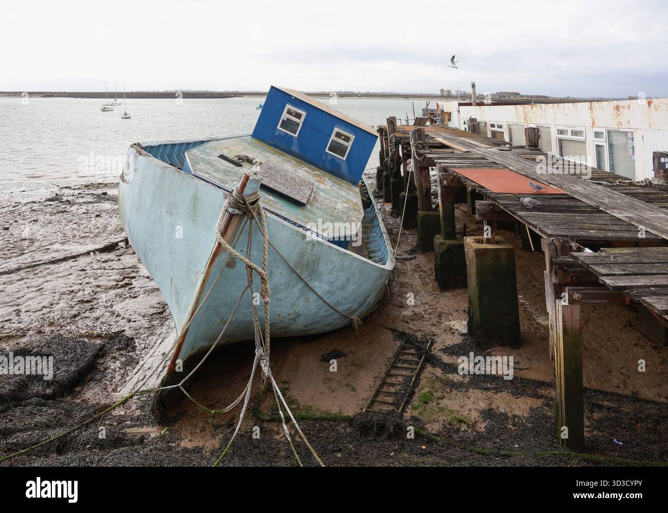 Bateau échoué à marée basse à côté d'une vieille jetée en bois, Burnham sur Crouch, Essex, Angleterre. Banque D'Images