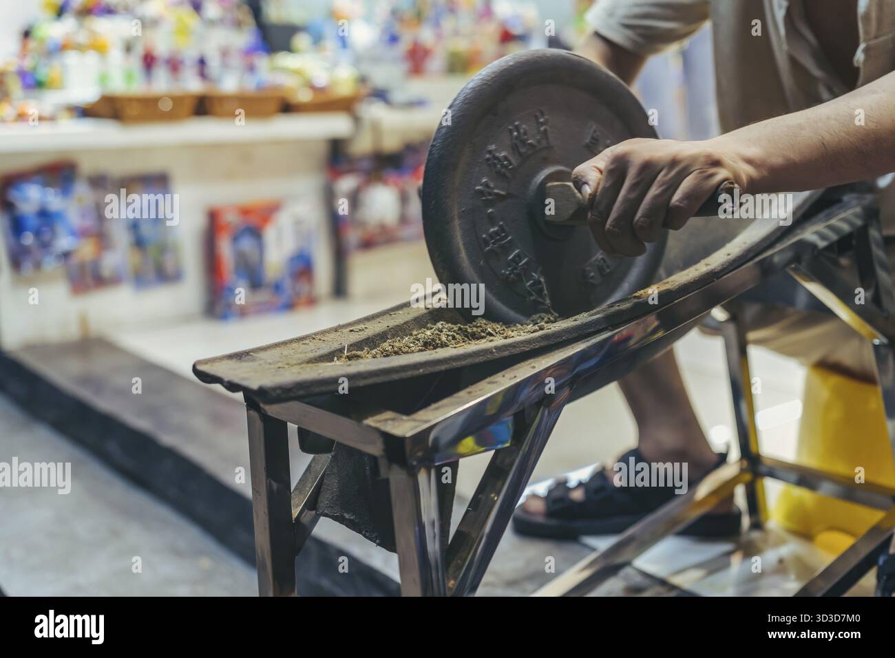 Feng Huang, Chine - août 2019 : homme roulant un outil rond lourd avec des poignées et écrasant la matière organique à l'intérieur d'une forme dans un petit atelier de souvenirs Banque D'Images