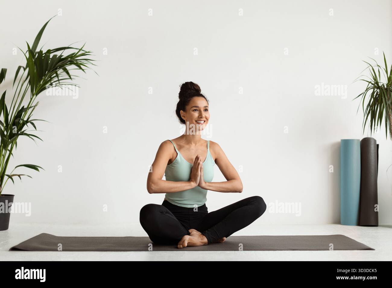 Jeune belle femme méditant dans la position Lotus sur le tapis de fitness dans l'espace studio paisible Banque D'Images