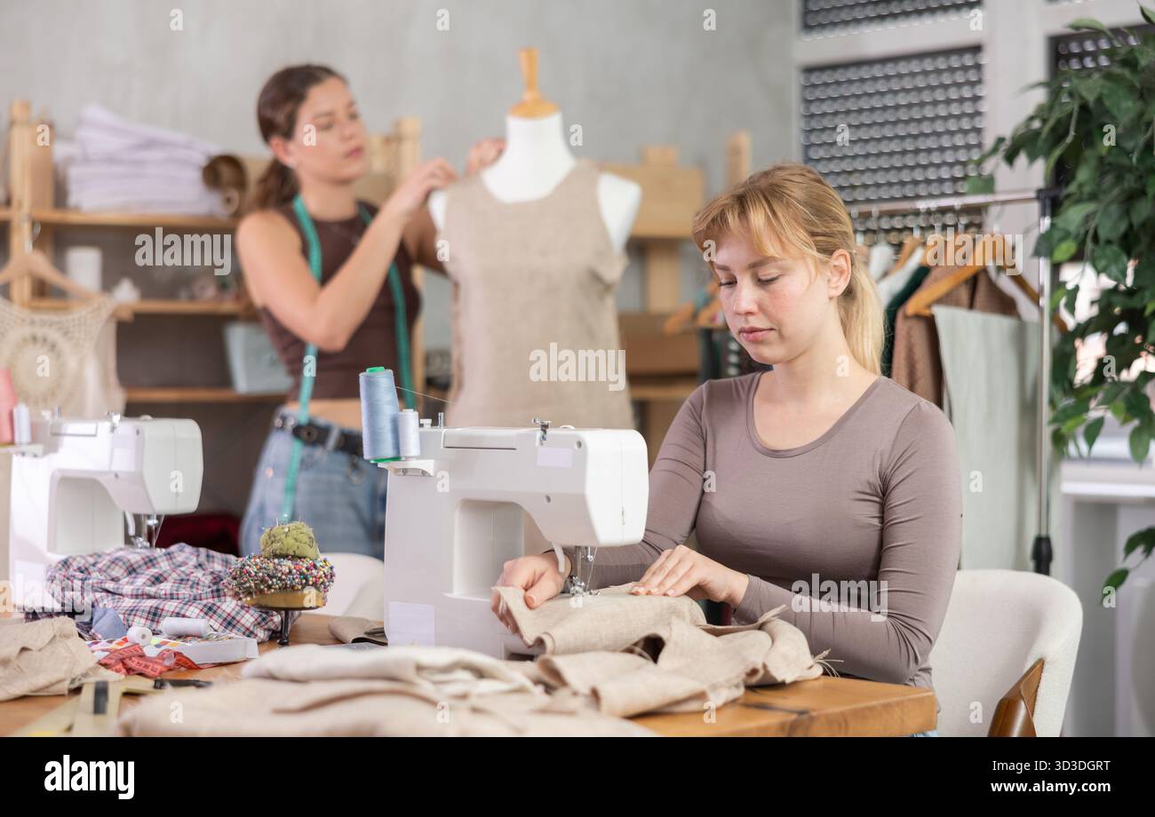 Tailleur femme travaillant sur une machine à coudre avec un assistant en arrière-plan Banque D'Images