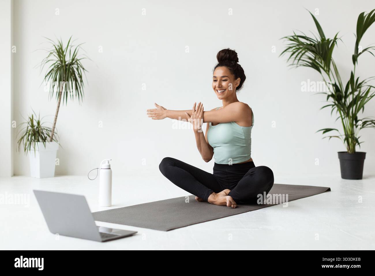 Belle jeune femme s'étire à la maison pendant la formation en ligne dans Activewear Banque D'Images