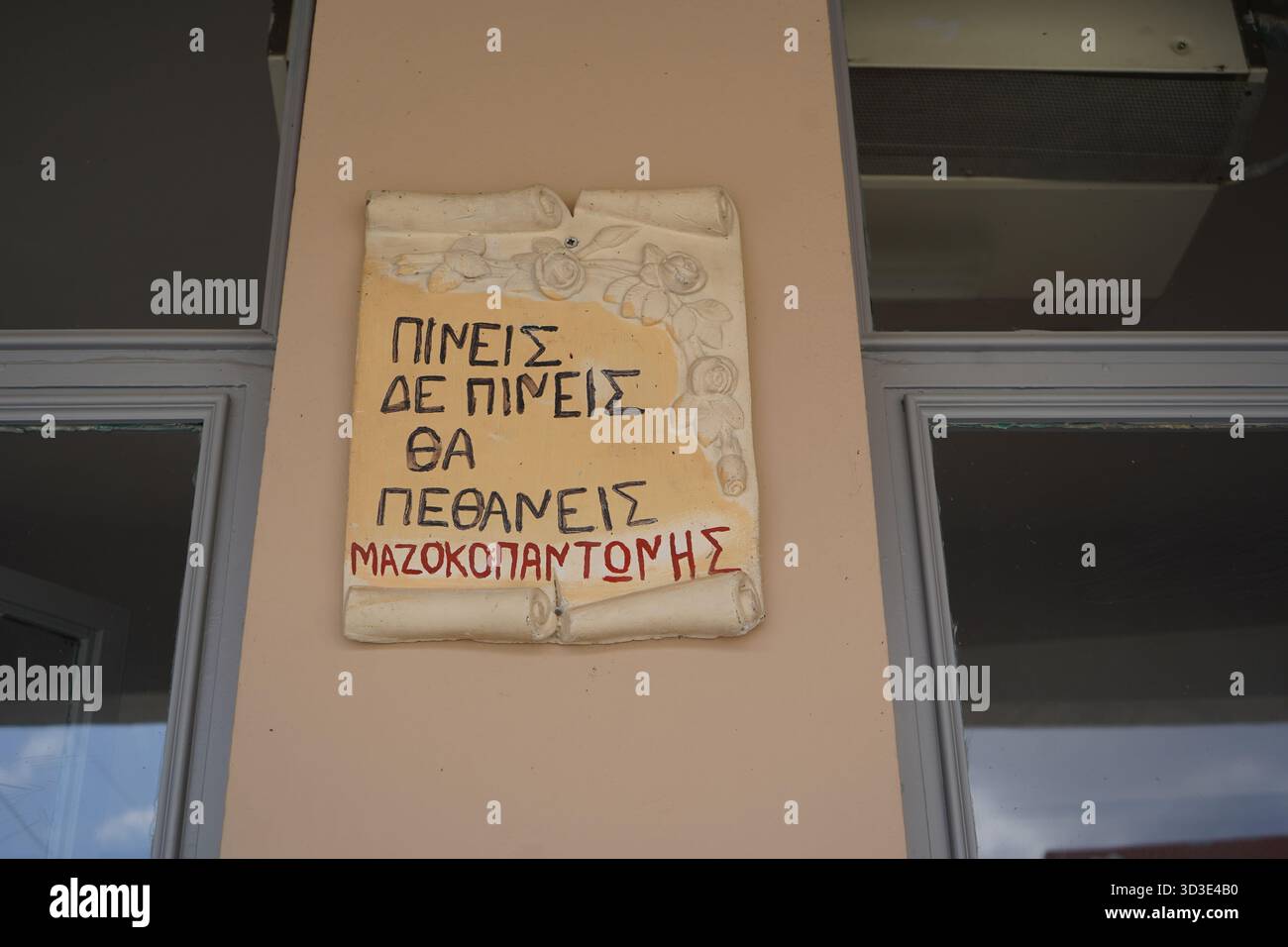 Panneau en céramique sur un mur de kafeneio dans le village d'Apomarmas, signé 'Mazokopantonis', avec le dicton grec humoristique : vous buvez, vous ne buvez pas, vous mourrez. Banque D'Images