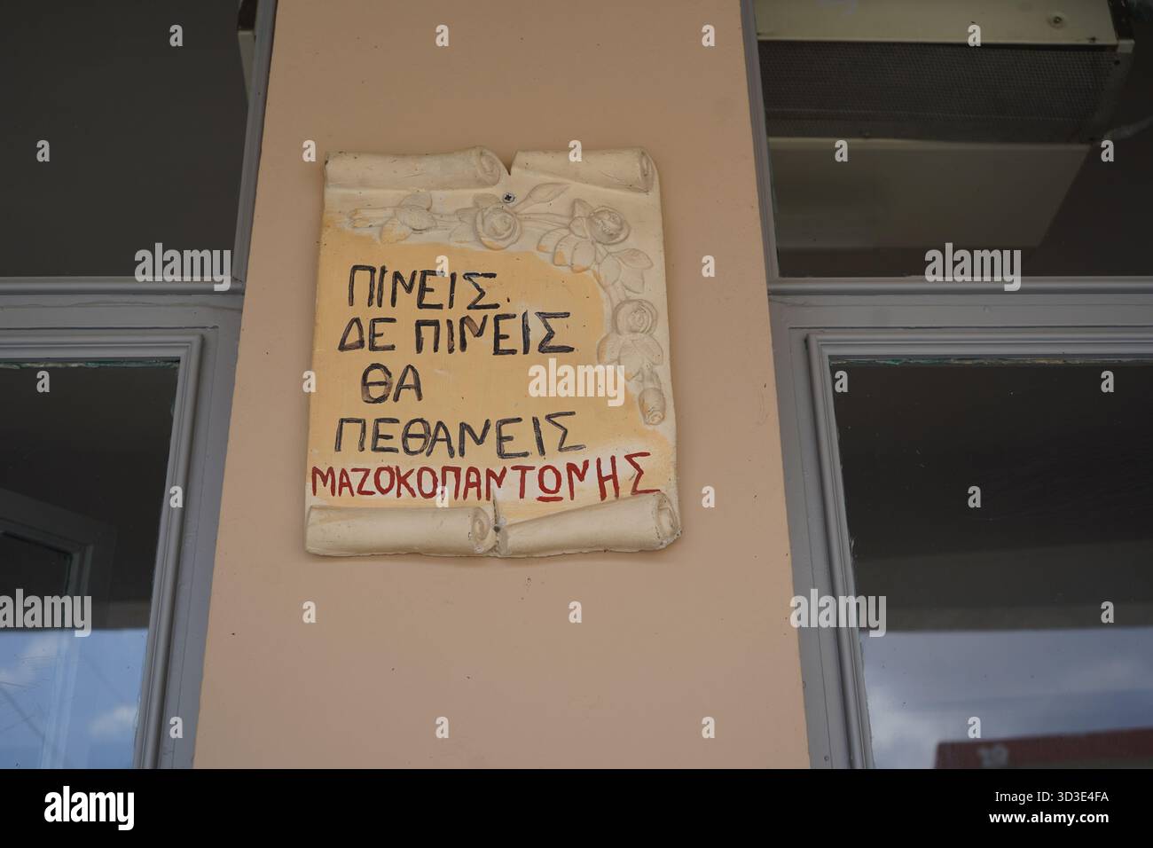 Panneau en céramique sur un mur de kafeneio dans le village d'Apomarmas, signé 'Mazokopantonis', avec le dicton grec humoristique : vous buvez, vous ne buvez pas, vous mourrez. Banque D'Images