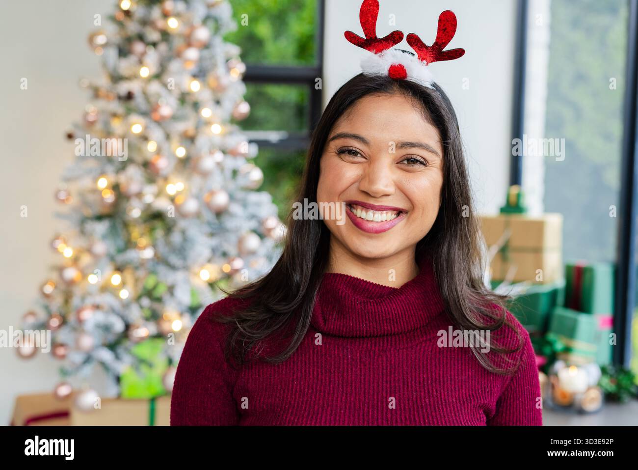 Femme asiatique souriante portant bandeau de bois debout dans le salon par arbre givré près des cadeaux Banque D'Images