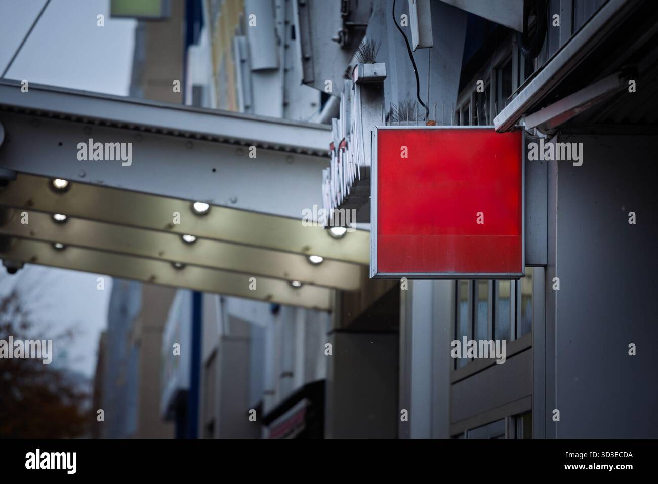 Un panneau carré rouge blanc de boîte lumineuse est suspendu à une façade commerciale sur une rue nord-américaine, sous des auvents métalliques et de petites lampes. panneau vide pr Banque D'Images