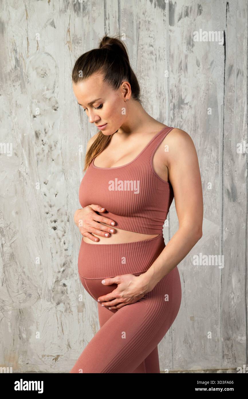 Femme enceinte embrassant la maternité et le bien-être, tenant doucement son ventre grandissant dans des vêtements de fitness Banque D'Images