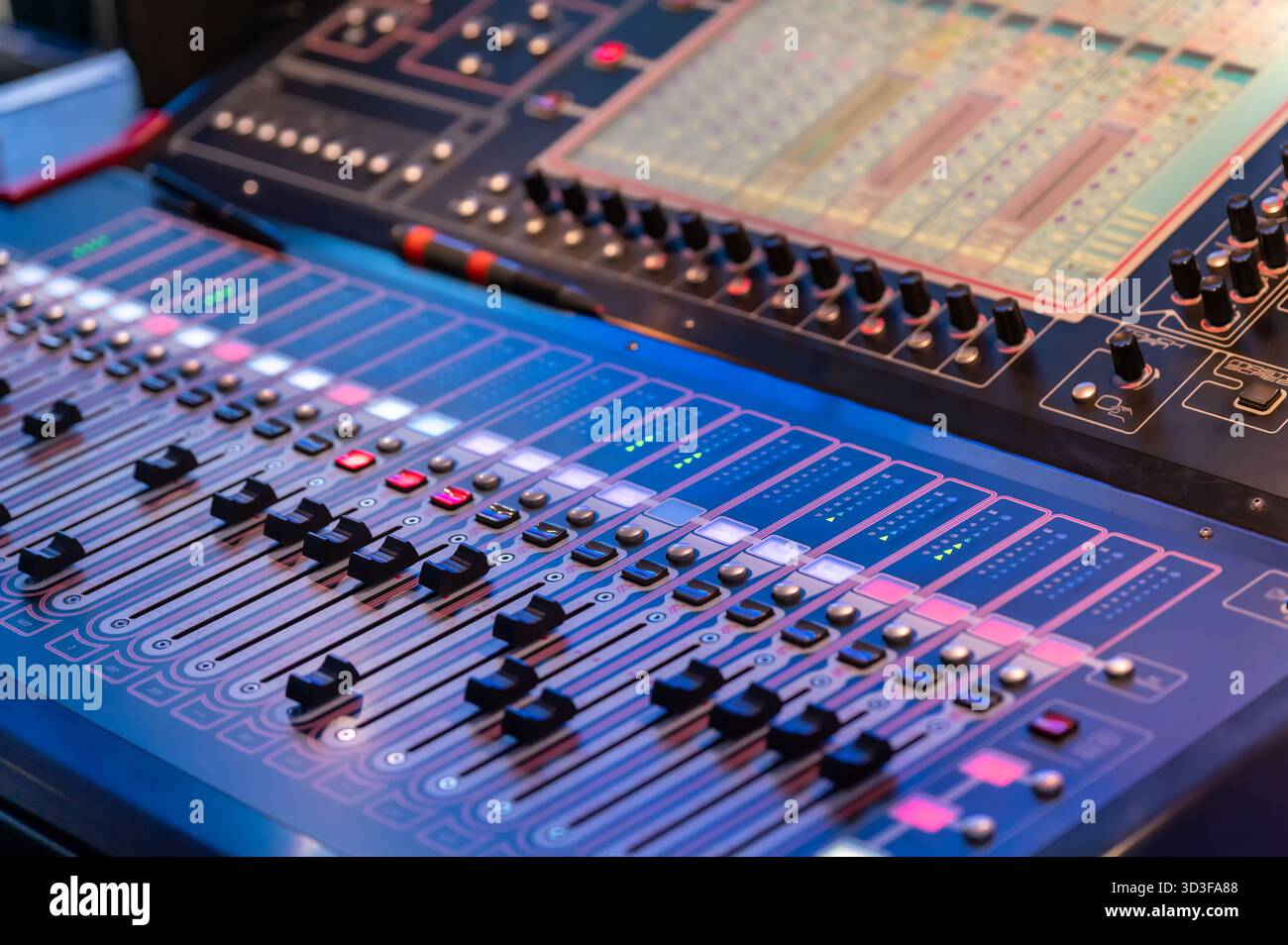 Gros plan d'une console de mixage avec boutons et faders lumineux, créant une atmosphère vibrante dans un cadre de production musicale Banque D'Images